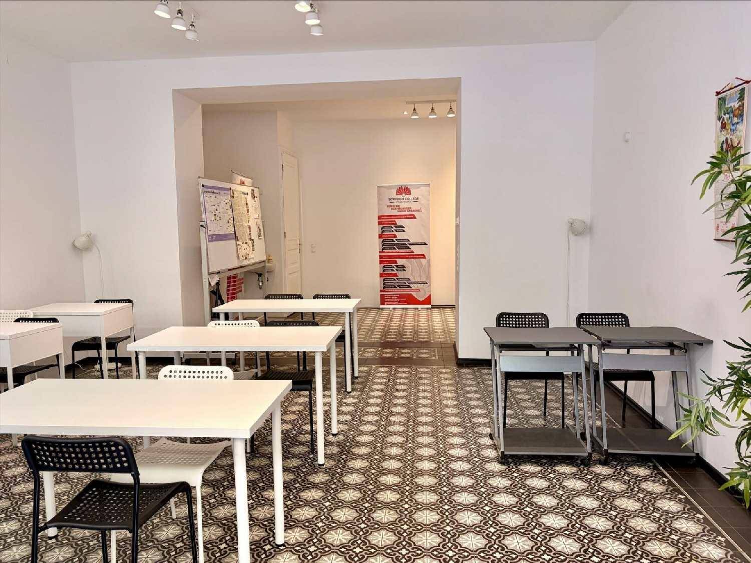 Weiterer Blick in den hellen Klassenraum mit mehreren Tischen und Stühlen, der zu einem hinteren Bereich führt.