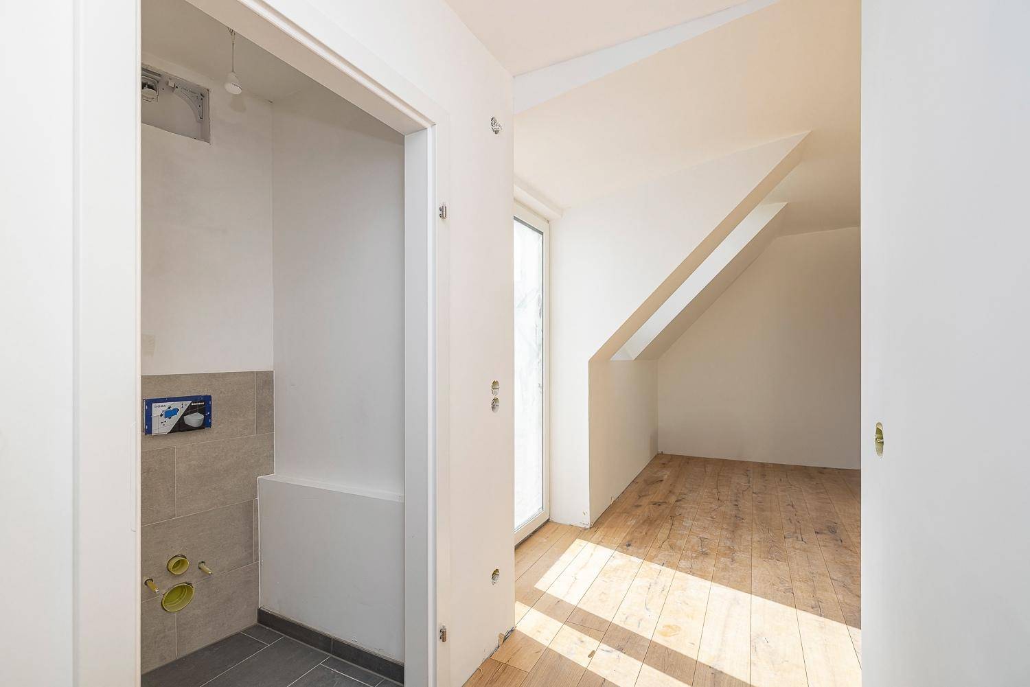 Heller Flur mit Holzboden und Zugang zu einem vorbereiteten WC-Bereich.
