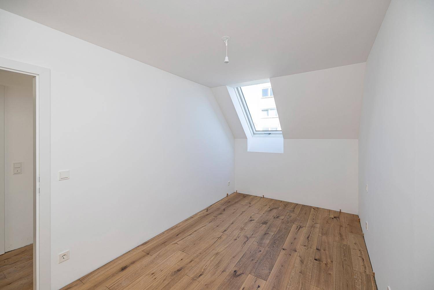 Schlafzimmer im Dachgeschoss mit Holzboden, Dachschräge und einem Dachfenster für natürliches Licht.