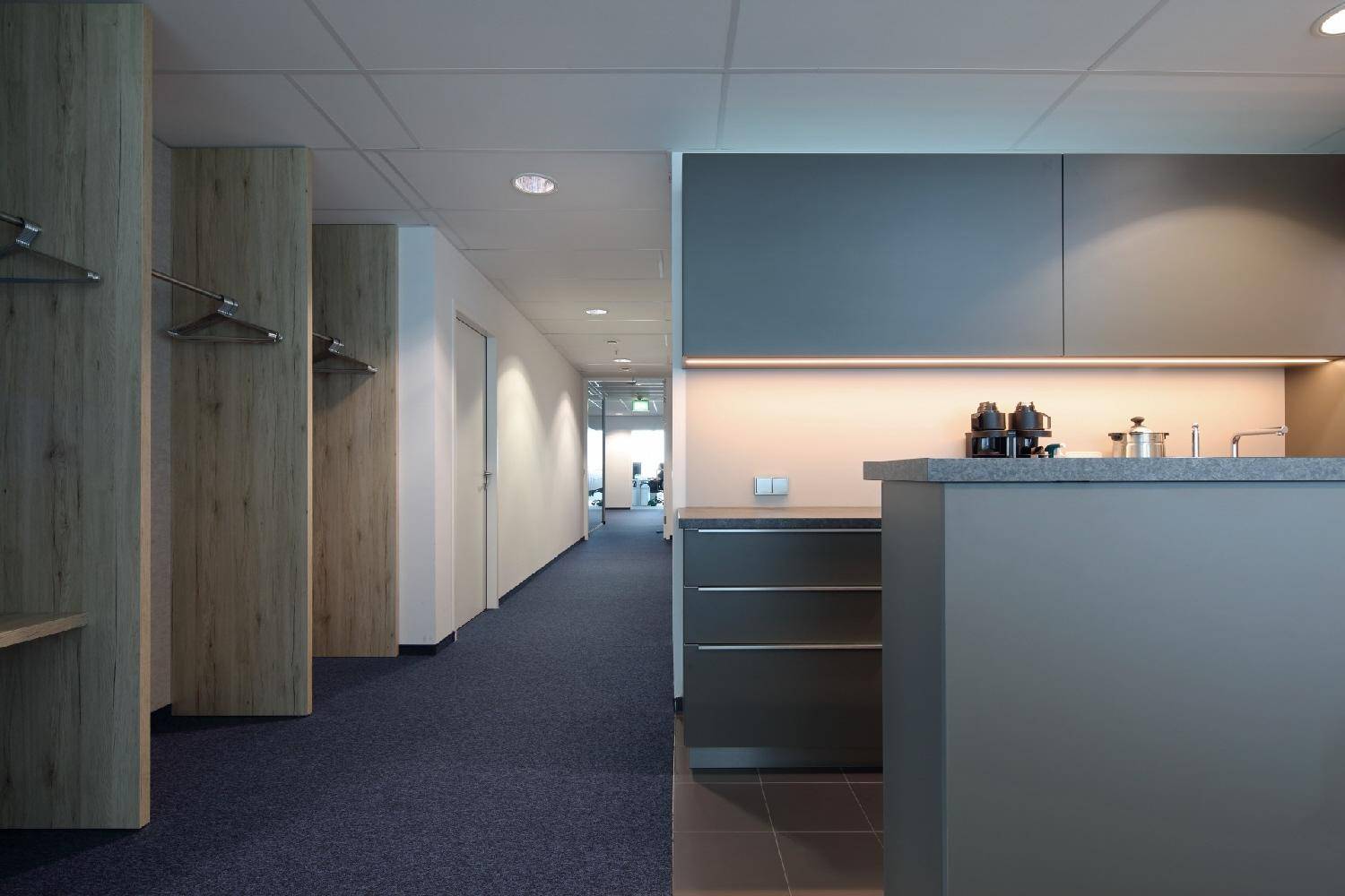 Moderner Bürogang mit Holzelementen, Teppichboden und einer integrierten Küchenzeile.