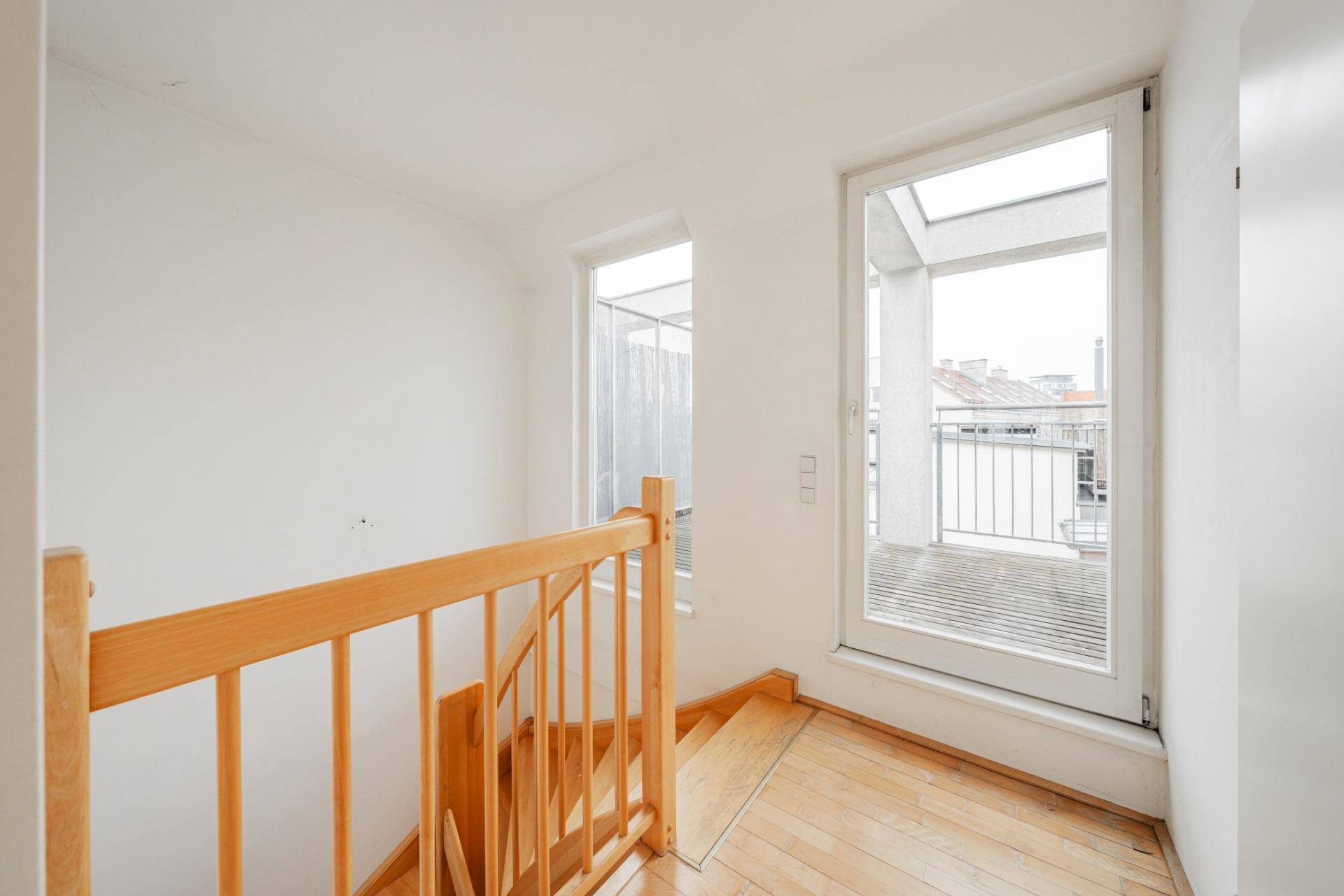 Heller Treppenabsatz mit Holztreppe und Zugang zu einem Balkon durch eine große Glastür.