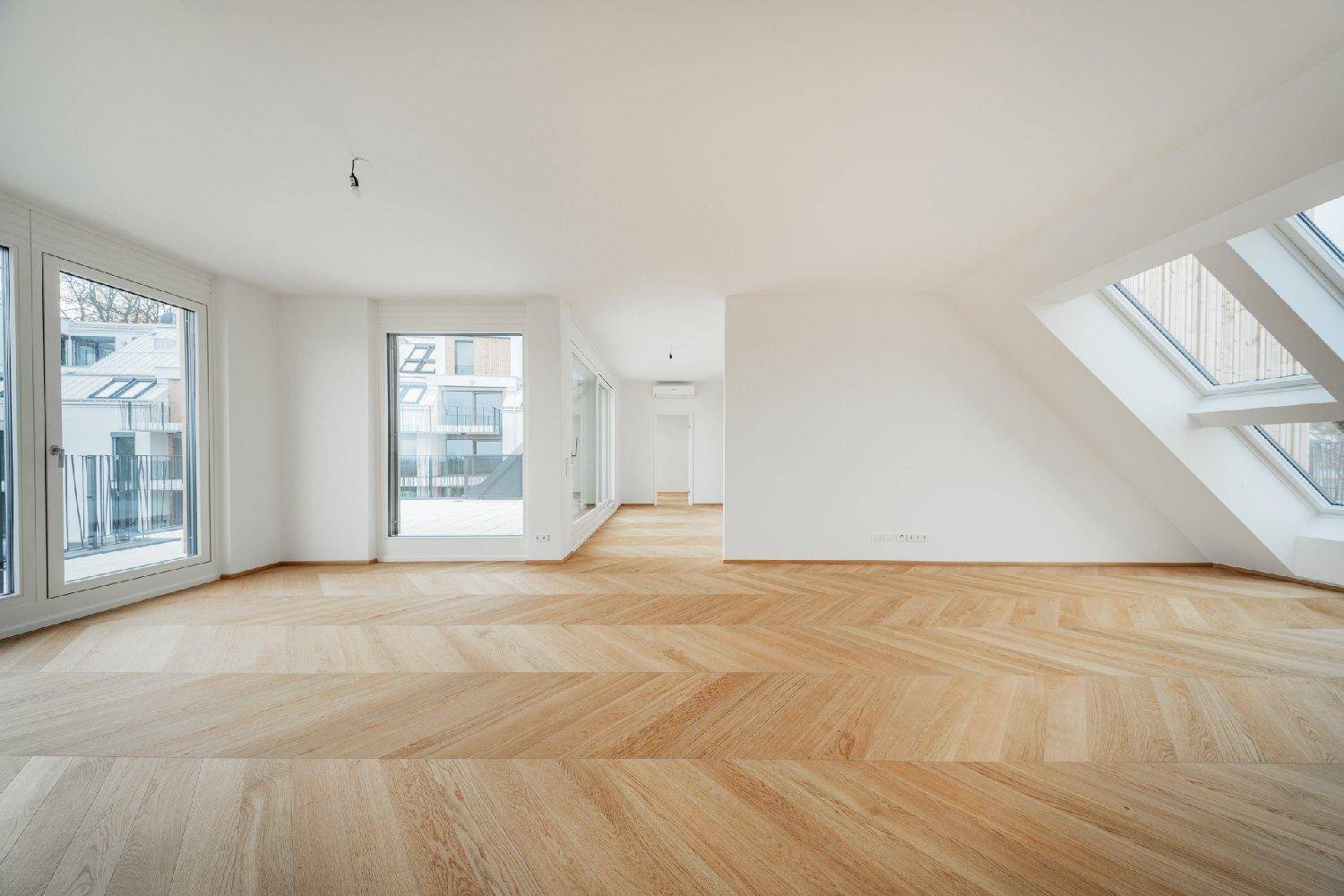 Geräumiges, helles Zimmer mit elegantem Fischgrätparkett und großen Dachfenstern im Neubau.
