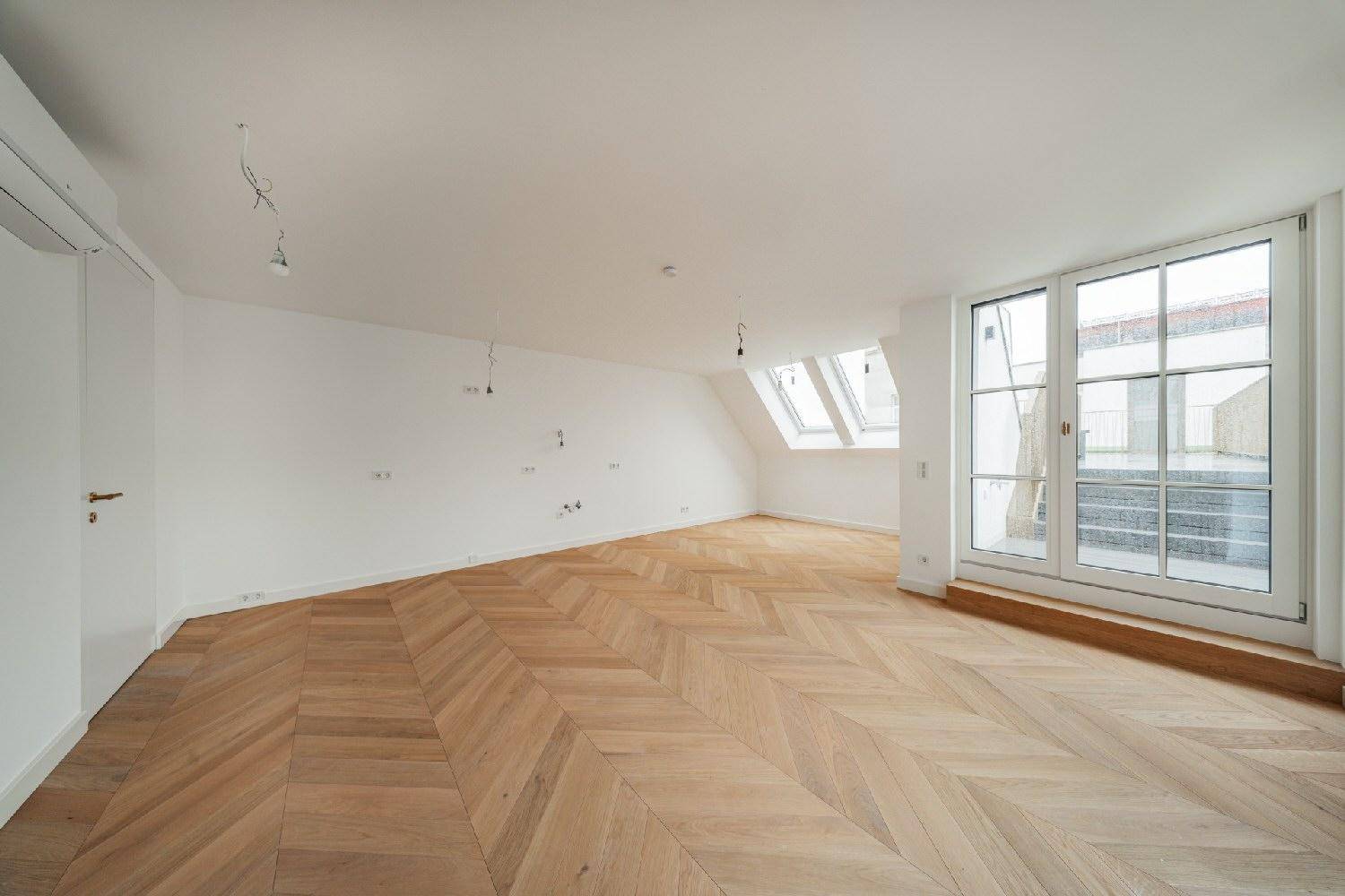 Geräumiges Zimmer mit elegantem Fischgrätparkett, Dachfenstern und weiß gestrichenen Wänden.