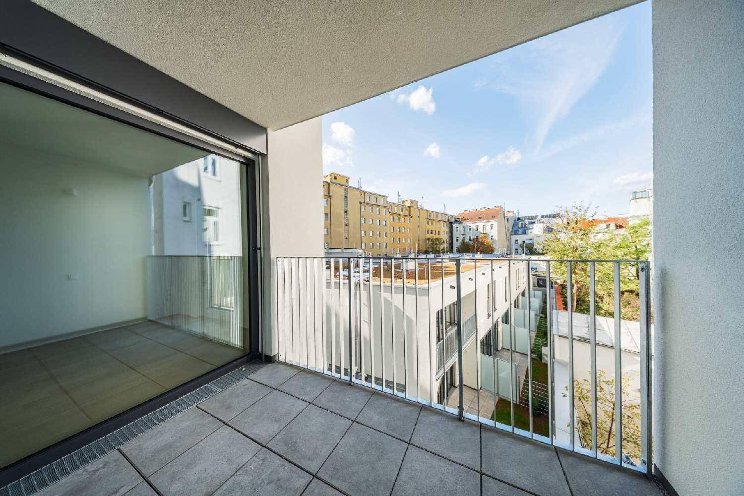 Heller Balkon mit Fliesenboden und Blick auf die umliegenden Gebäude und den Himmel.