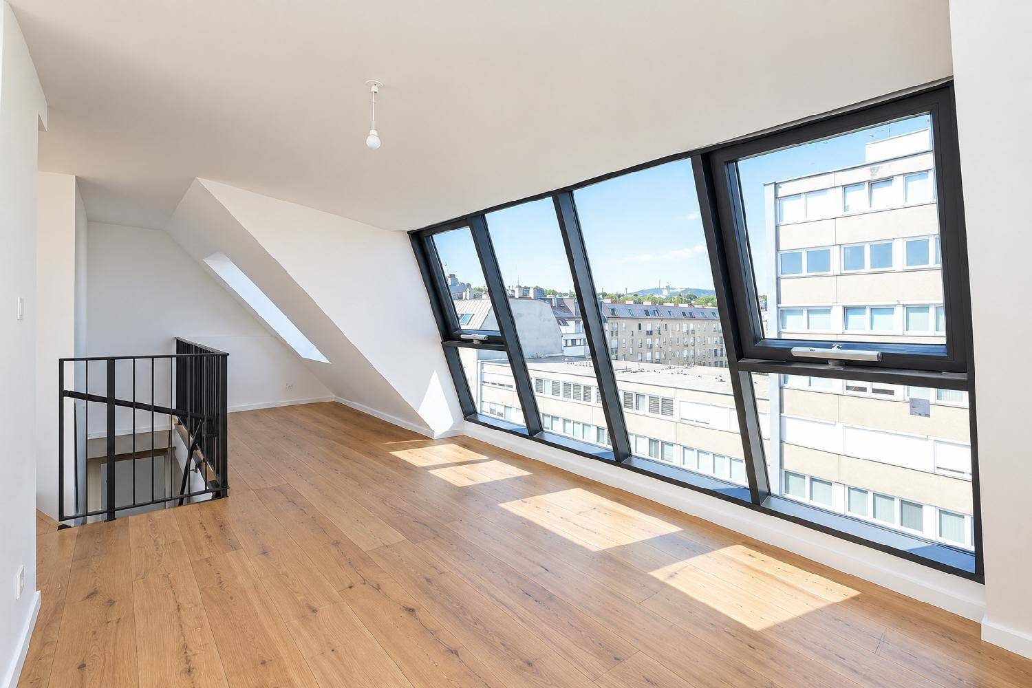 Heller Raum im Dachgeschoss mit schrägen Fenstern und Holzboden, bietet einen weiten Stadtblick.