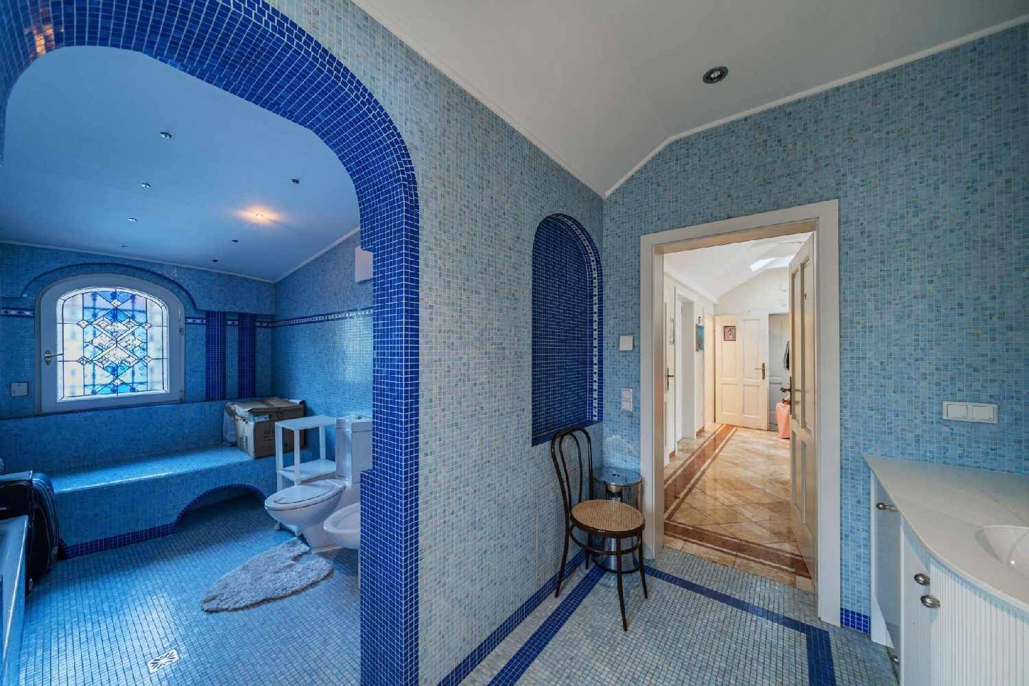 Blau gefliestes Badezimmer mit Bidet, Toilette und einem dekorativen Buntglasfenster.