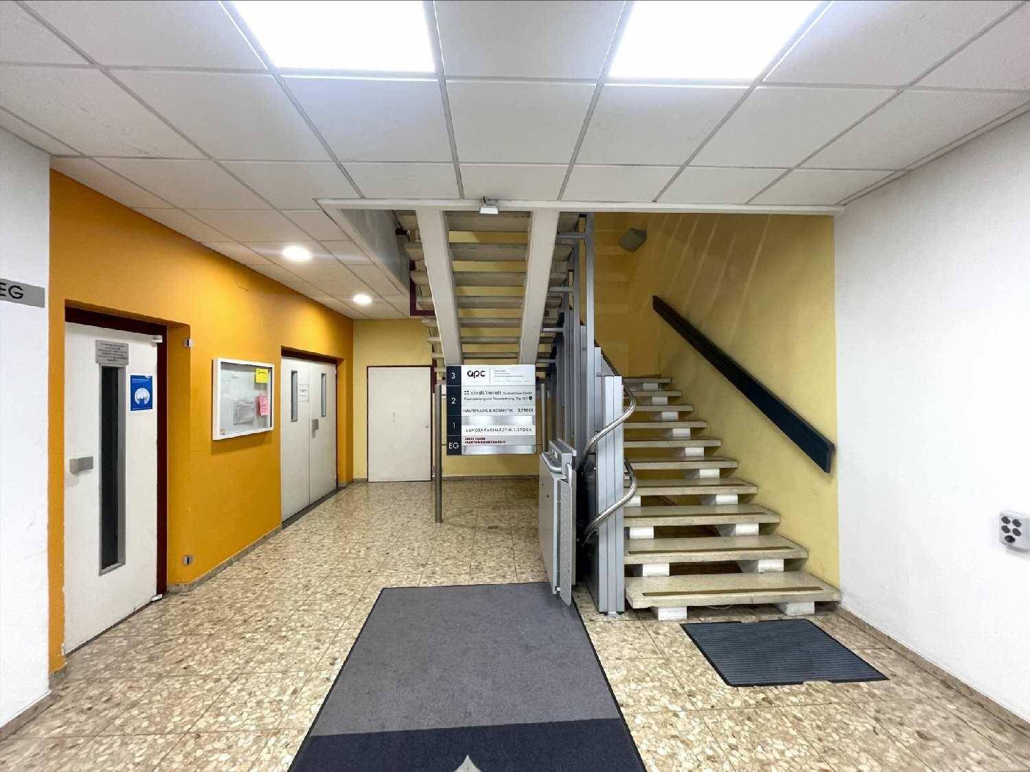 Eingangsbereich mit Treppe, Rollstuhlrampe und Aufzug, gekennzeichnet durch gelbe und weiße Wände.