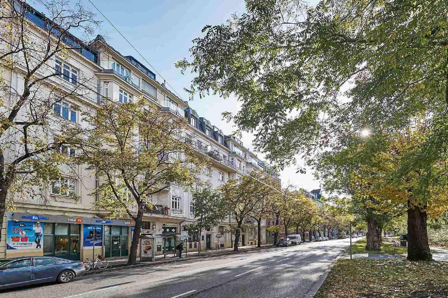 Historisches Gebäude mit vielen Fenstern und Balkonen entlang einer belebten Straße mit Bäumen.