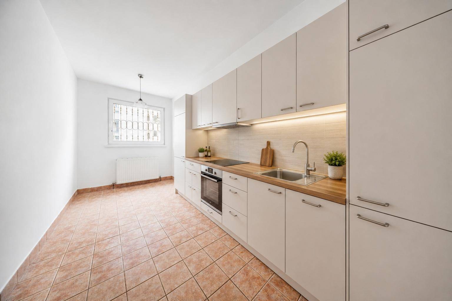 Moderne Einbauküche mit hellen Schränken, Holzarbeitsplatte und Terrakotta-Fliesenboden.