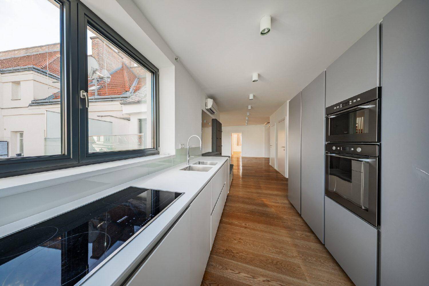 Lange, moderne Küche mit grauen Schränken, integrierten Geräten und Fenstern mit Stadtblick.