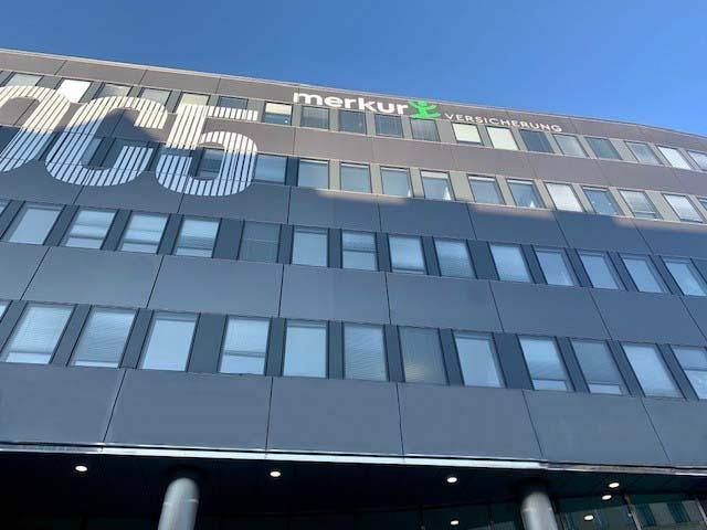 Oberer Teil eines modernen Bürogebäudes mit vielen Fenstern und einer großen "OC5"-Beschriftung an der Fassade.