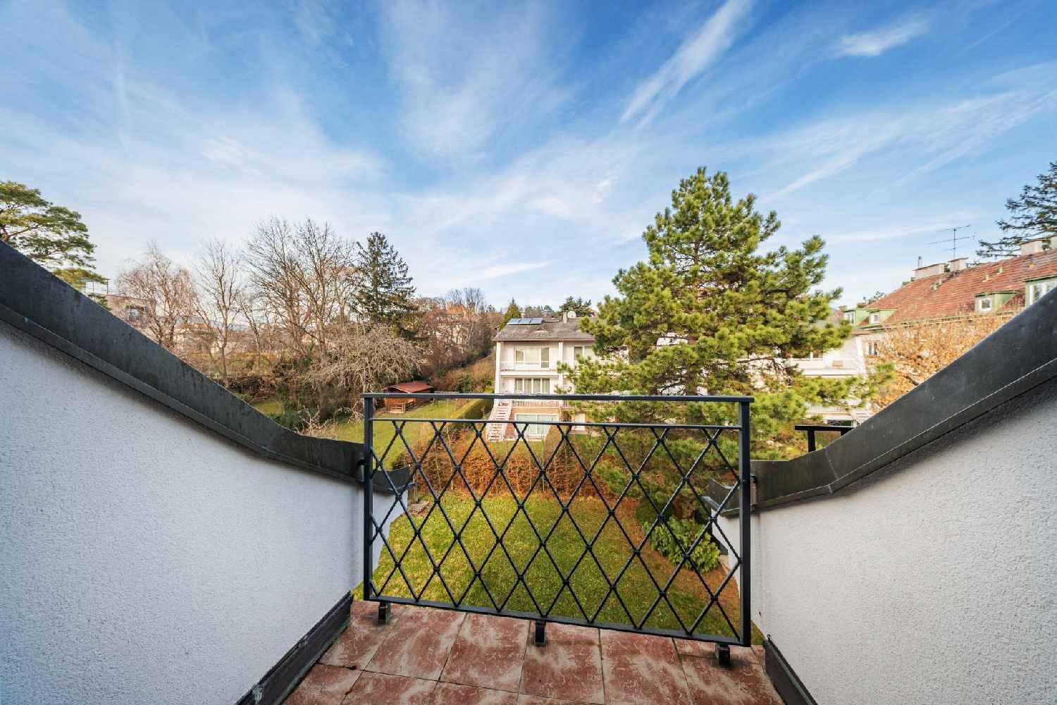 Kleiner Balkon mit schmiedeeisernem Geländer und Blick auf den grünen Gartenbereich und Bäume.
