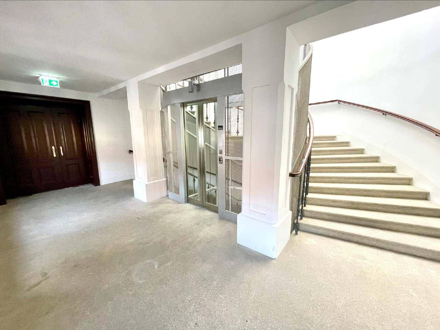 Heller Eingangsbereich mit geschwungener Treppe und modernem Glasaufzug.