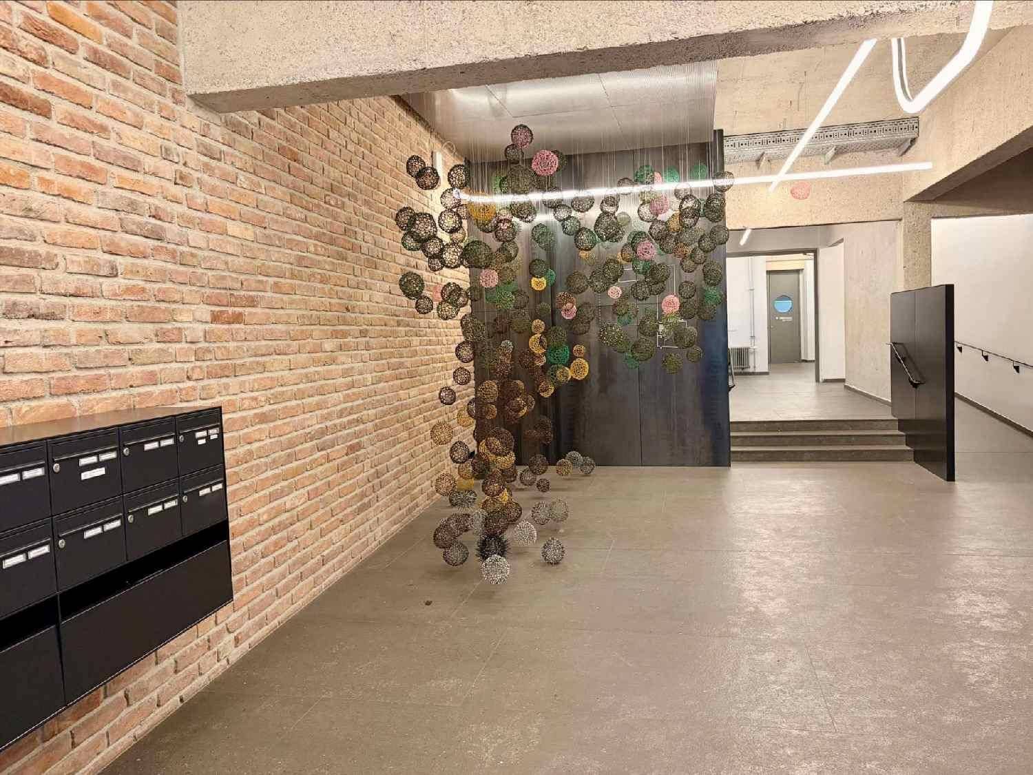 Moderner Eingangsbereich mit Ziegelwand, Briefkästen und künstlerischer Installation.