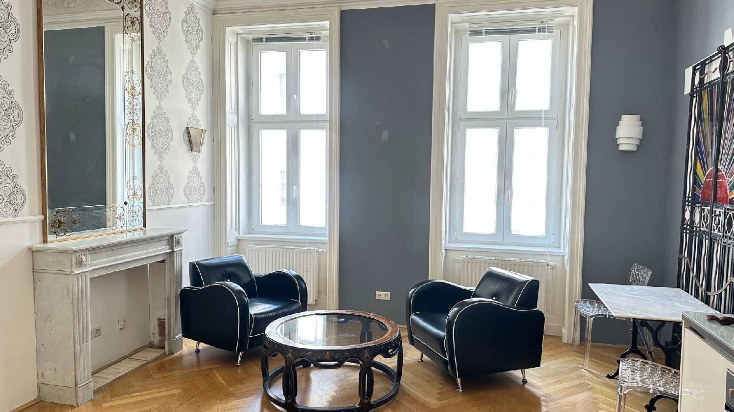Helles Wohnzimmer mit Fischgrätparkett, hohen Fenstern und klassischem Kaminsims.