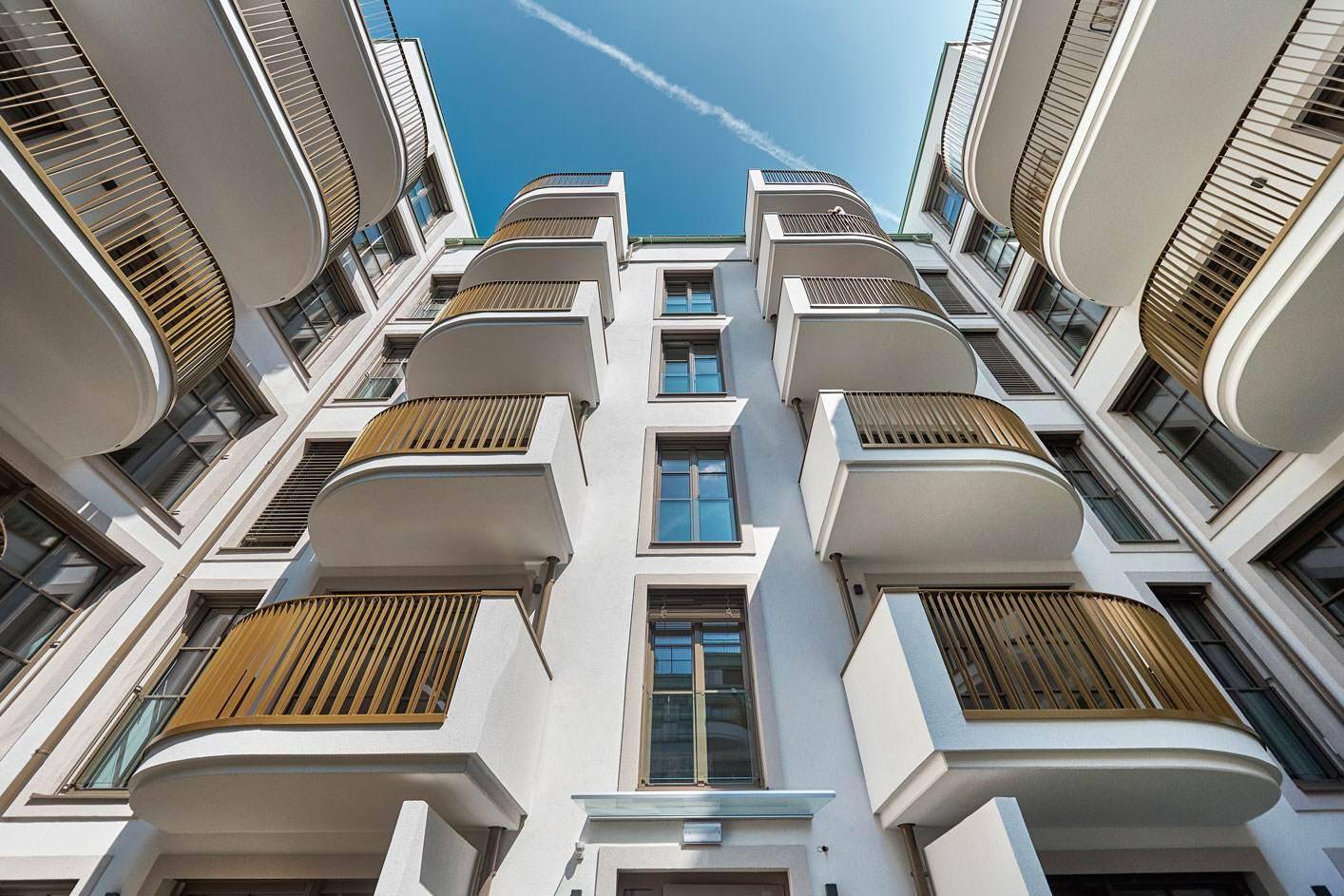Beeindruckende Fassade eines modernen Wohngebäudes mit geschwungenen Balkonen und goldenen Geländern.