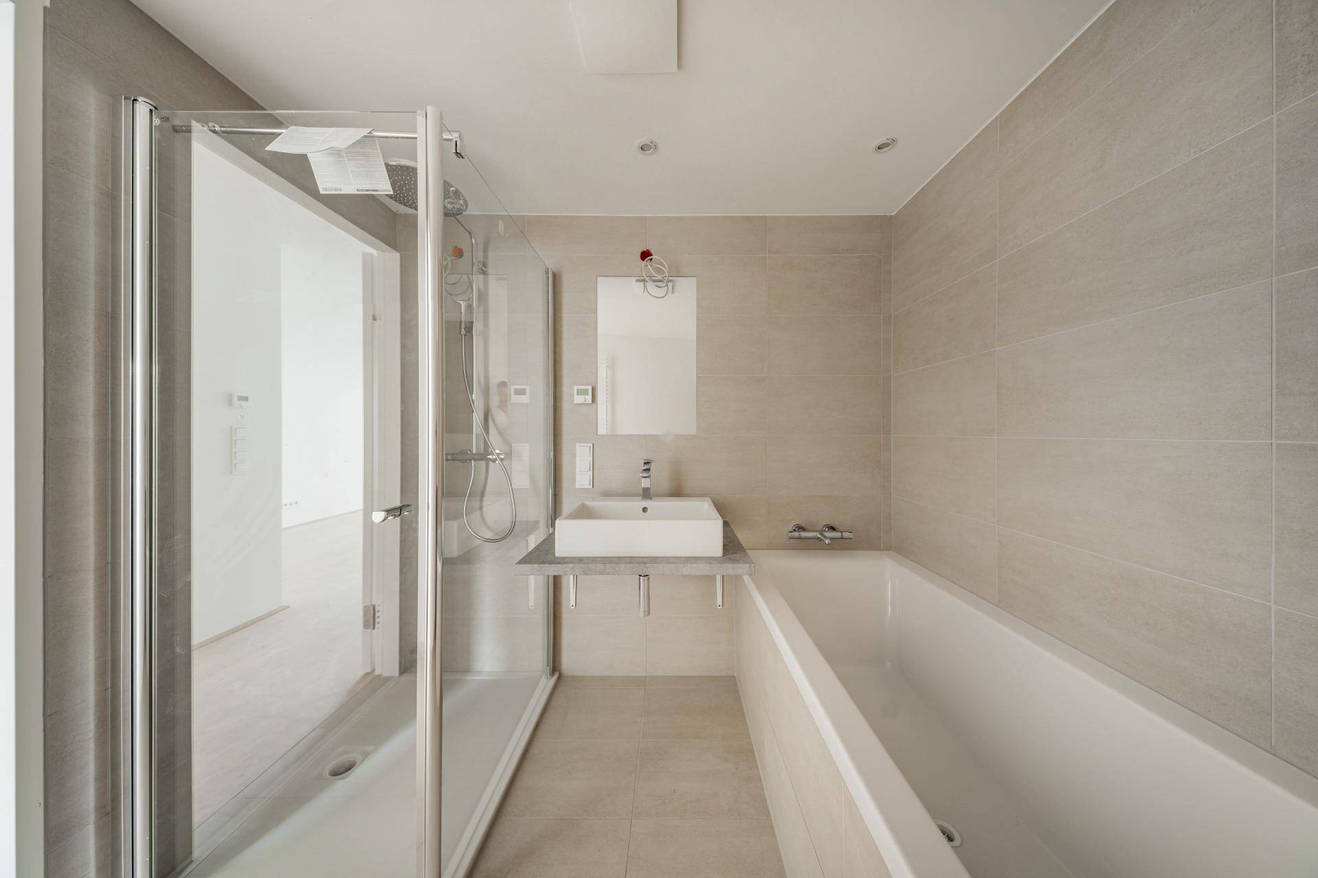 Modernes Badezimmer mit hellgrauen Fliesen, Badewanne, begehbarer Dusche und Einzelwaschbecken.