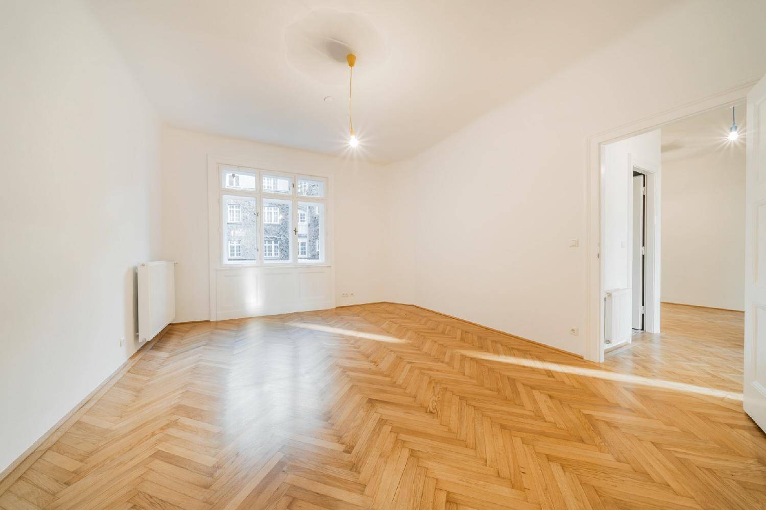 Helles Zimmer mit Fischgrätparkett und einem großen Fenster, das einen Blick auf die Umgebung bietet.