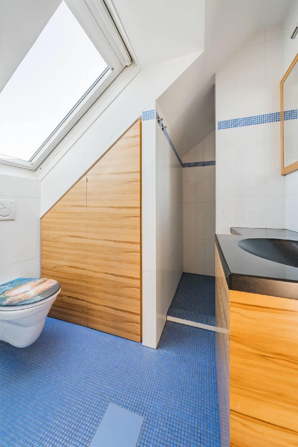 Badezimmer im Dachgeschoss mit WC, Dusche, Holzwaschtisch und Dachfenster.