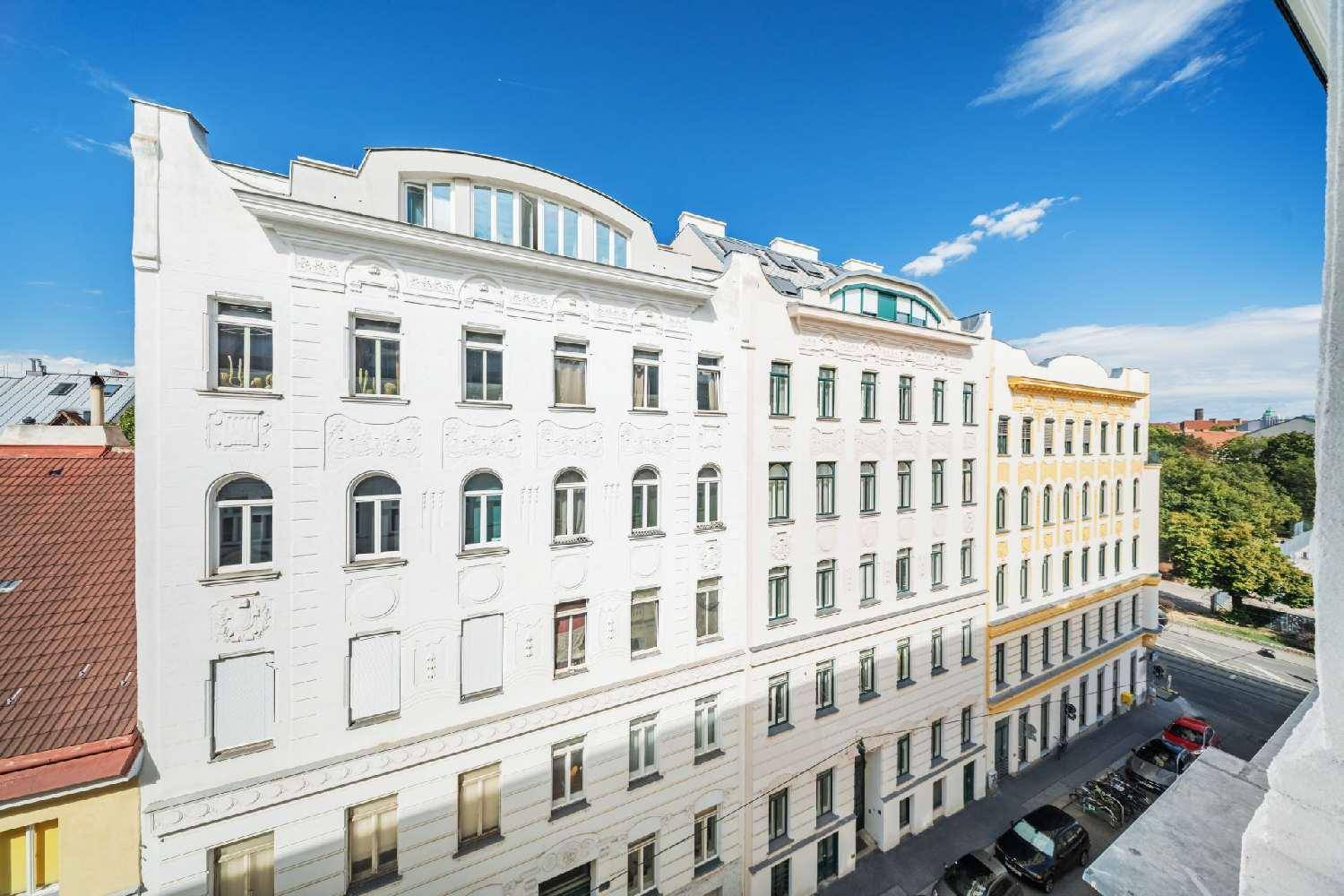 Historische Fassade eines Wohngebäudes mit vielen Fenstern und Dachaufbauten unter blauem Himmel.