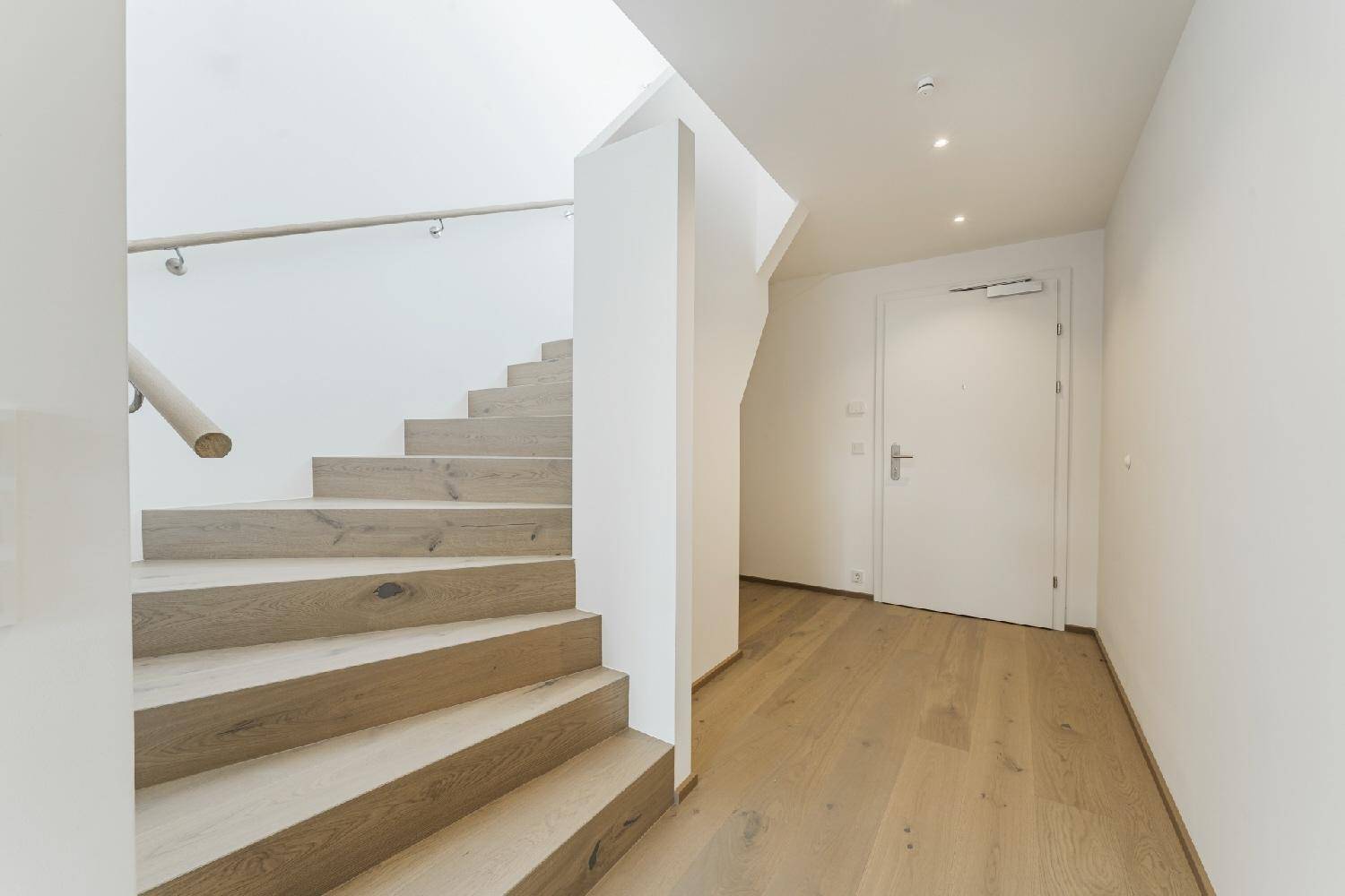 Moderner Flur mit Holztreppe und Eingangstür, ausgestattet mit hellem Holzboden.