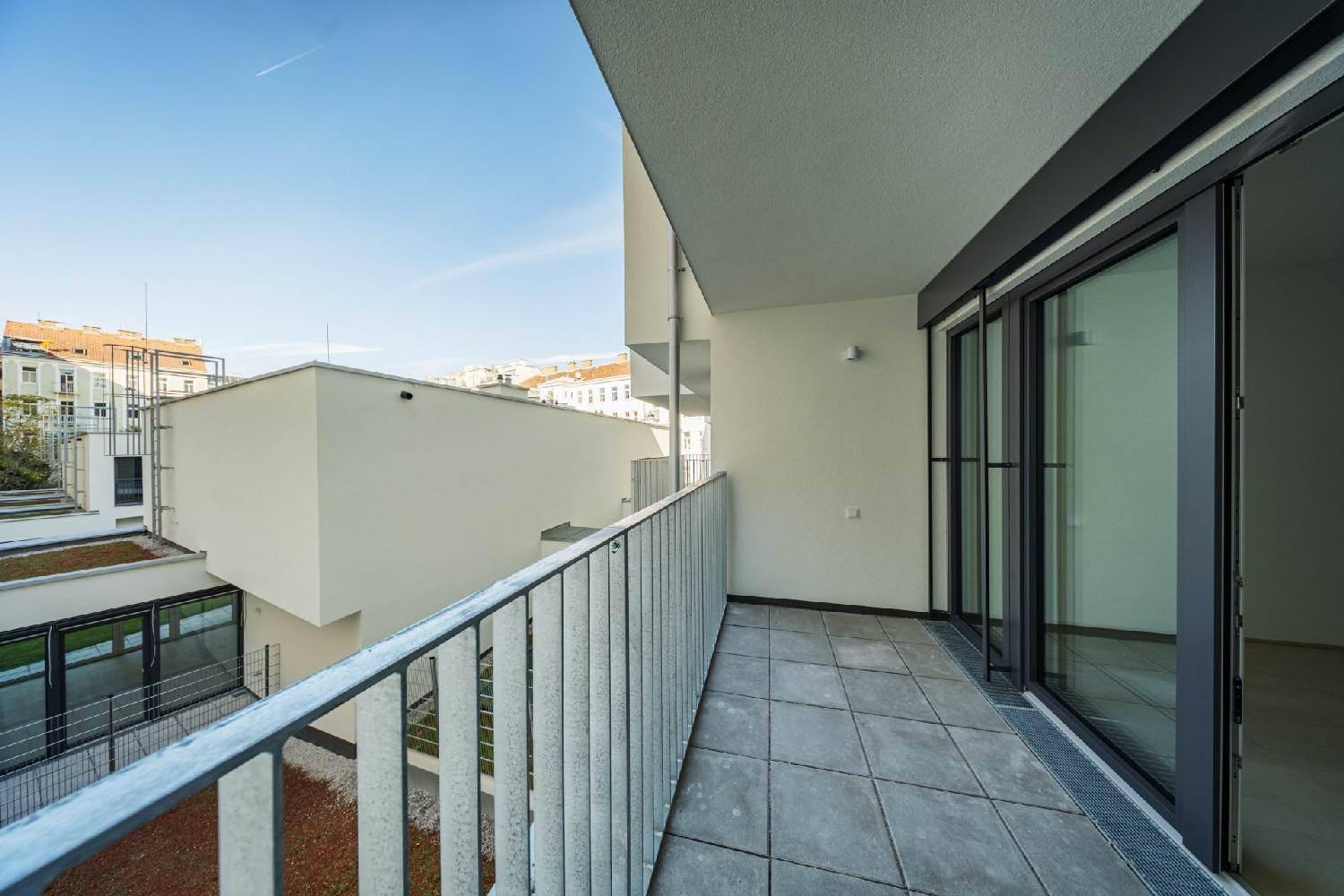 Geräumiger Balkon mit Fliesenboden und Metallgeländer, bietet einen Blick auf den Innenhof.
