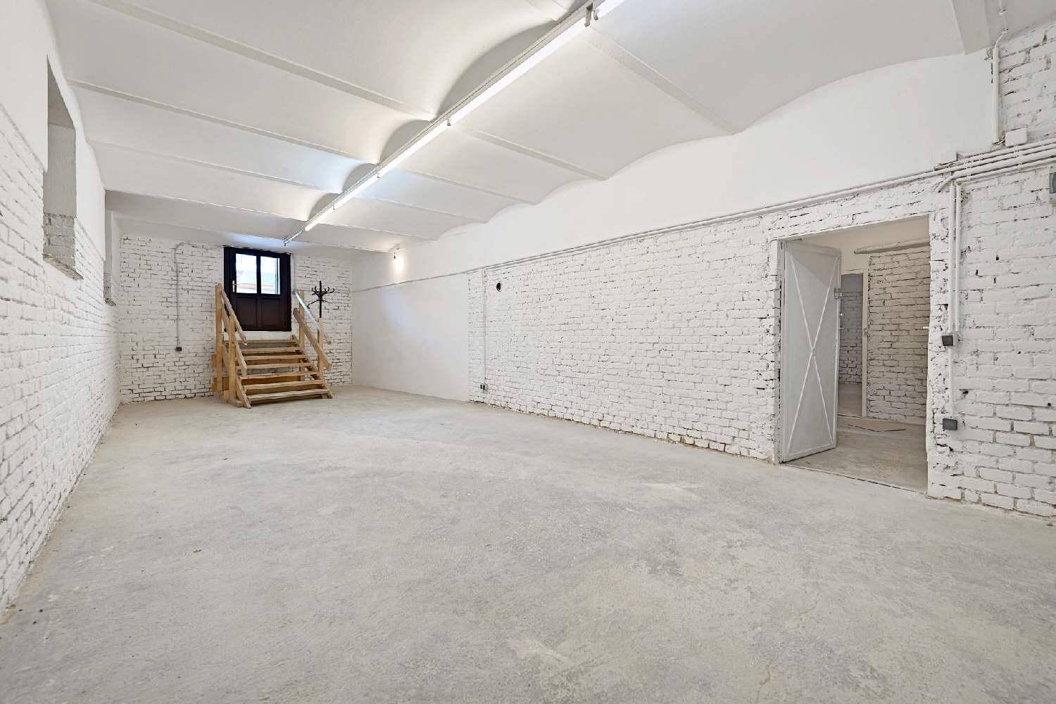 Geräumiger Lagerraum mit weiß gestrichenen Ziegelwänden, Betonboden und einer Holztreppe zum Ausgang.