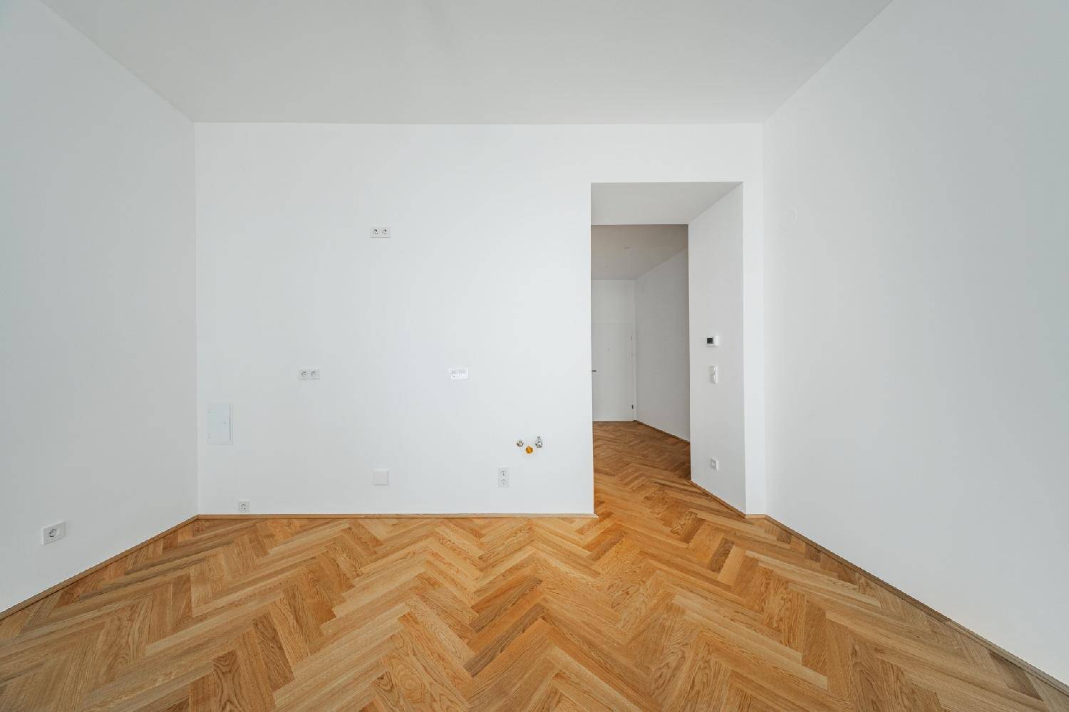 Leerer Raum mit Fischgrätparkett und Zugang zu einem weiteren Bereich.