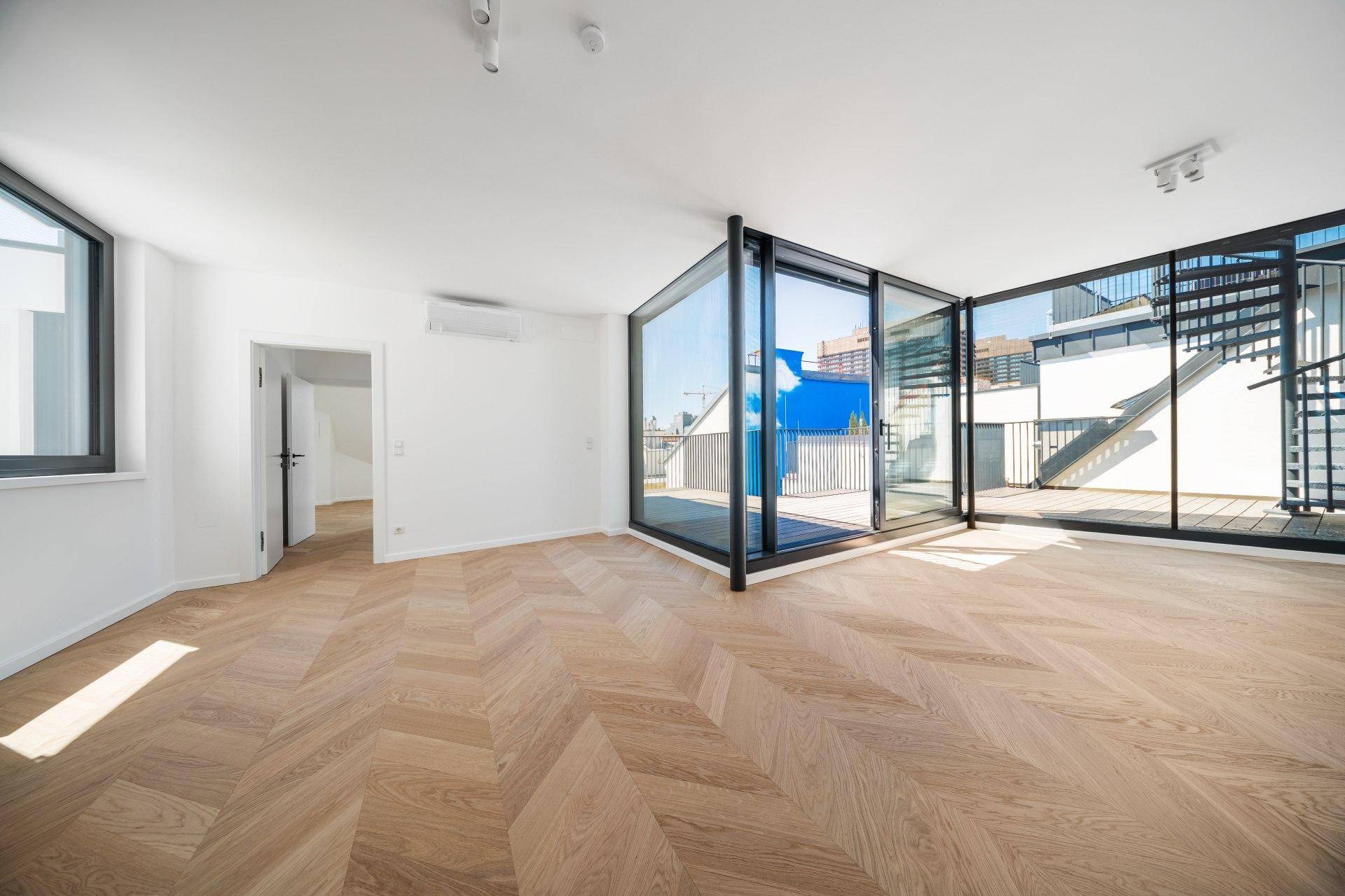 Geräumiger Wohnbereich mit Klimaanlage, Fischgrätparkett und direktem Zugang zur Dachterrasse.