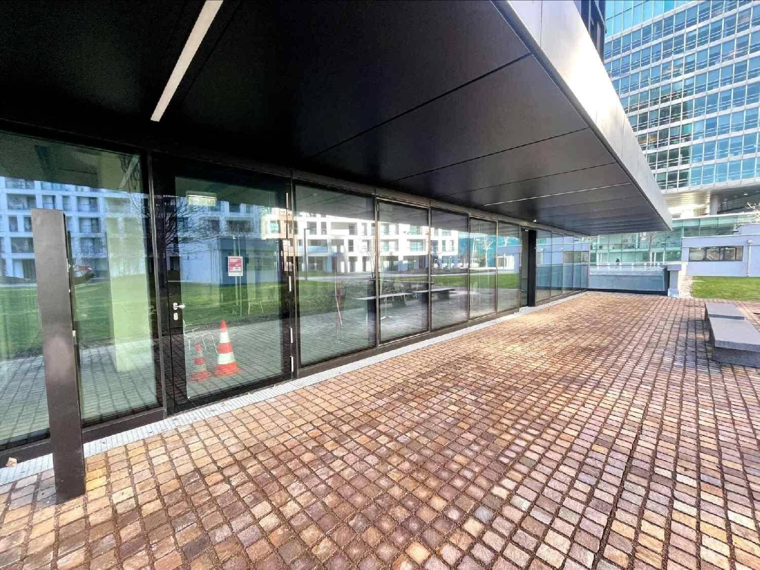 Eingangsbereich eines modernen Gebäudes mit großen Glasfronten und einem gepflasterten Vorplatz.