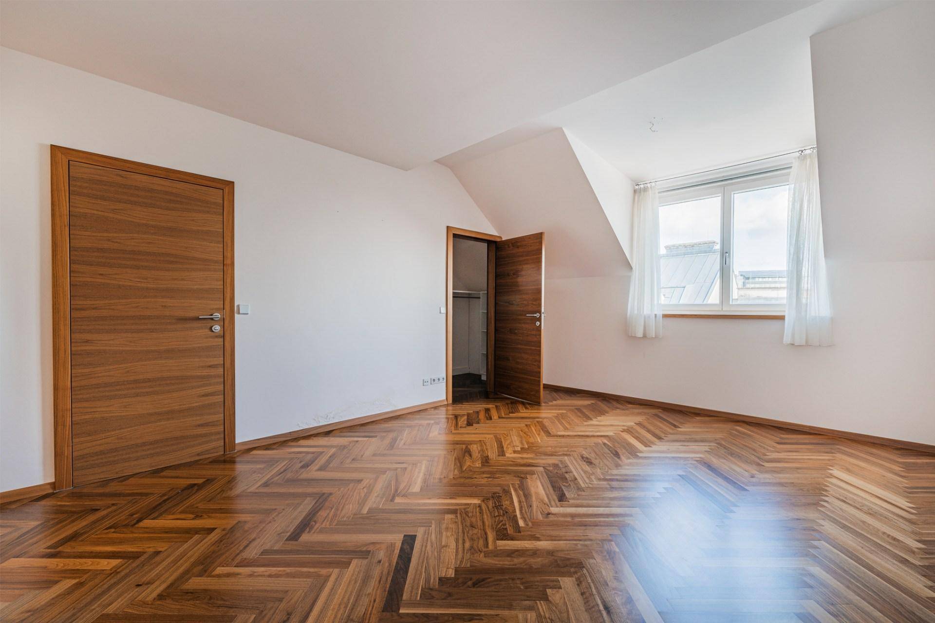 Geräumiges Schlafzimmer mit Fischgrätparkett, Dachschräge und Holztüren.