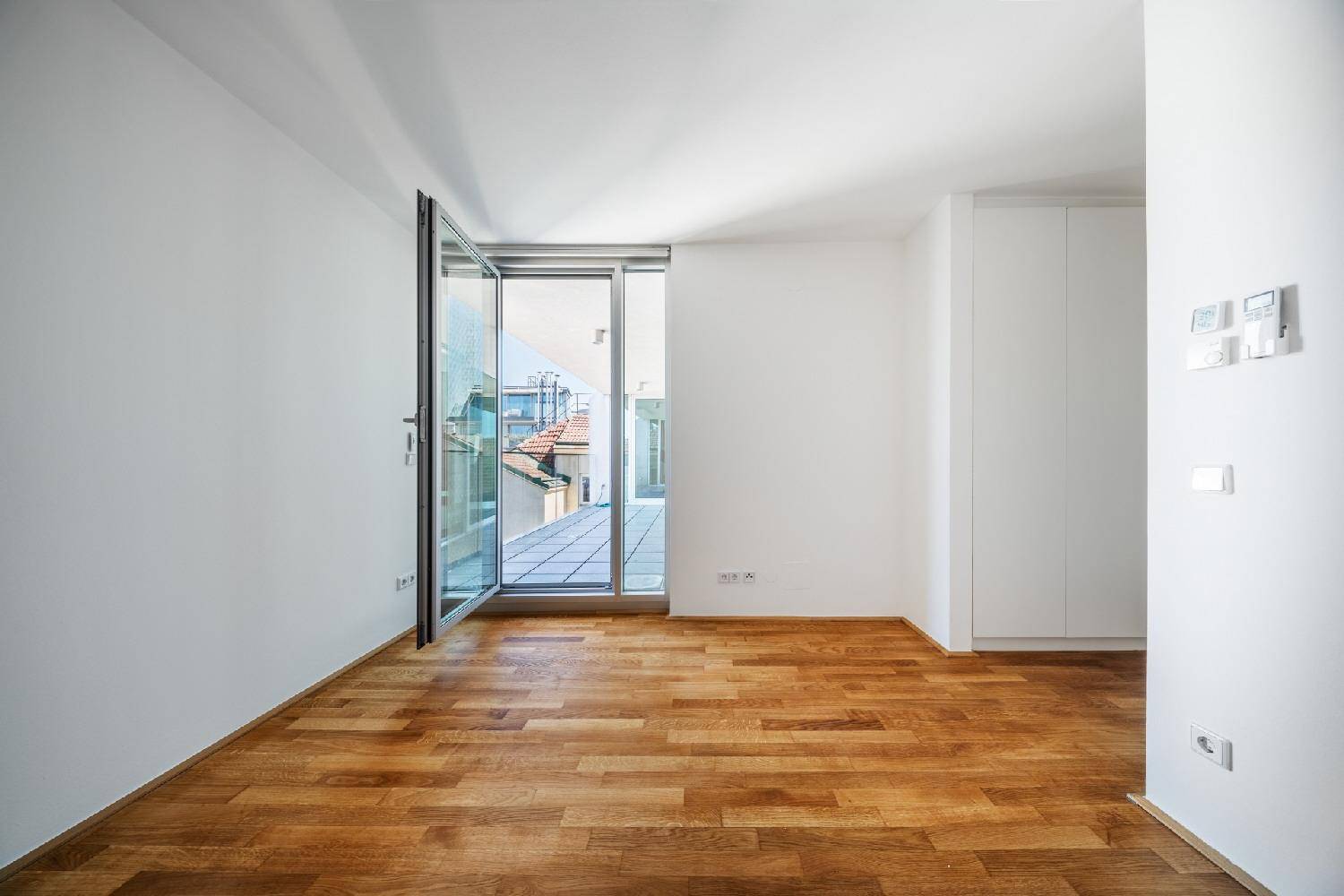 Heller Raum mit Holzboden, integrierten Schränken und Zugang zu einem sonnigen Außenbereich.