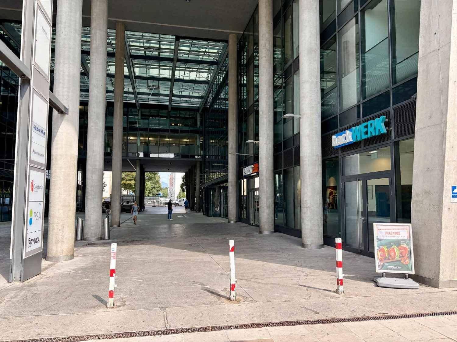 Moderner Eingangsbereich eines Bürogebäudes mit hohen Säulen und Glasdach, das viel Licht hereinlässt.