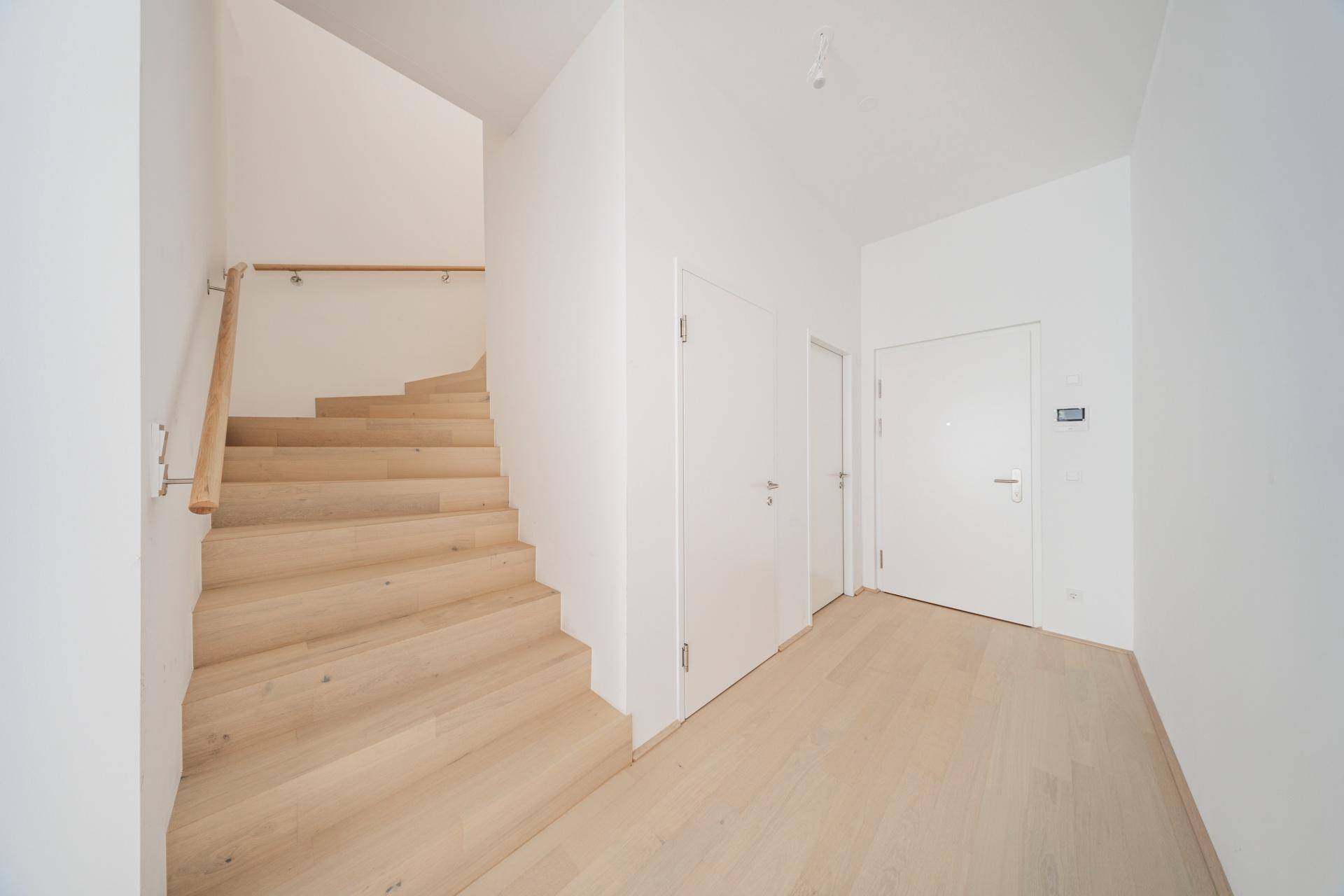 Heller Eingangsbereich mit einer modernen Holztreppe und passendem Holzboden.