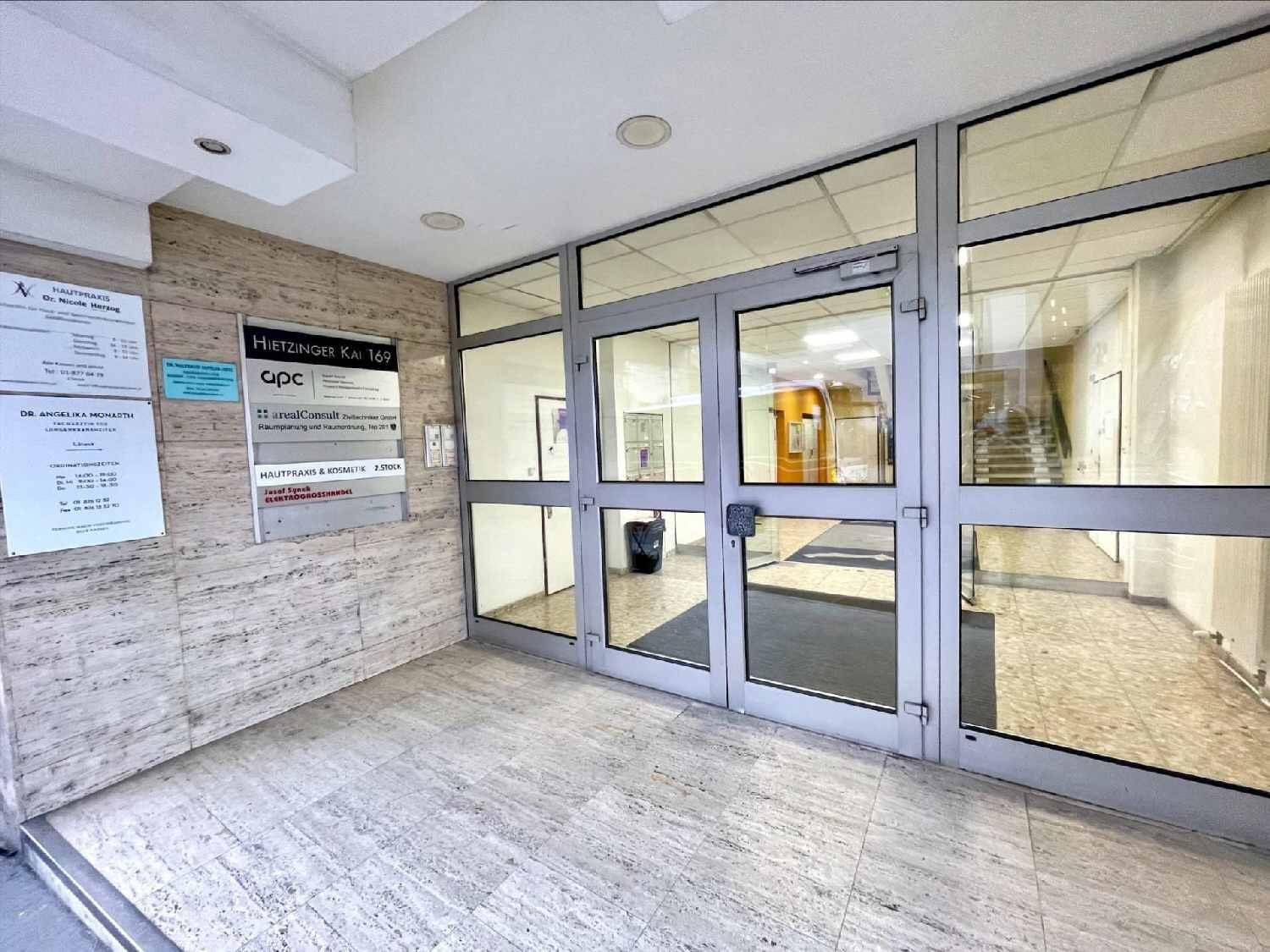Gebäudeeingang mit Glastüren und Steinfliesen an der Fassade, umgeben von Geschäftsschildern.