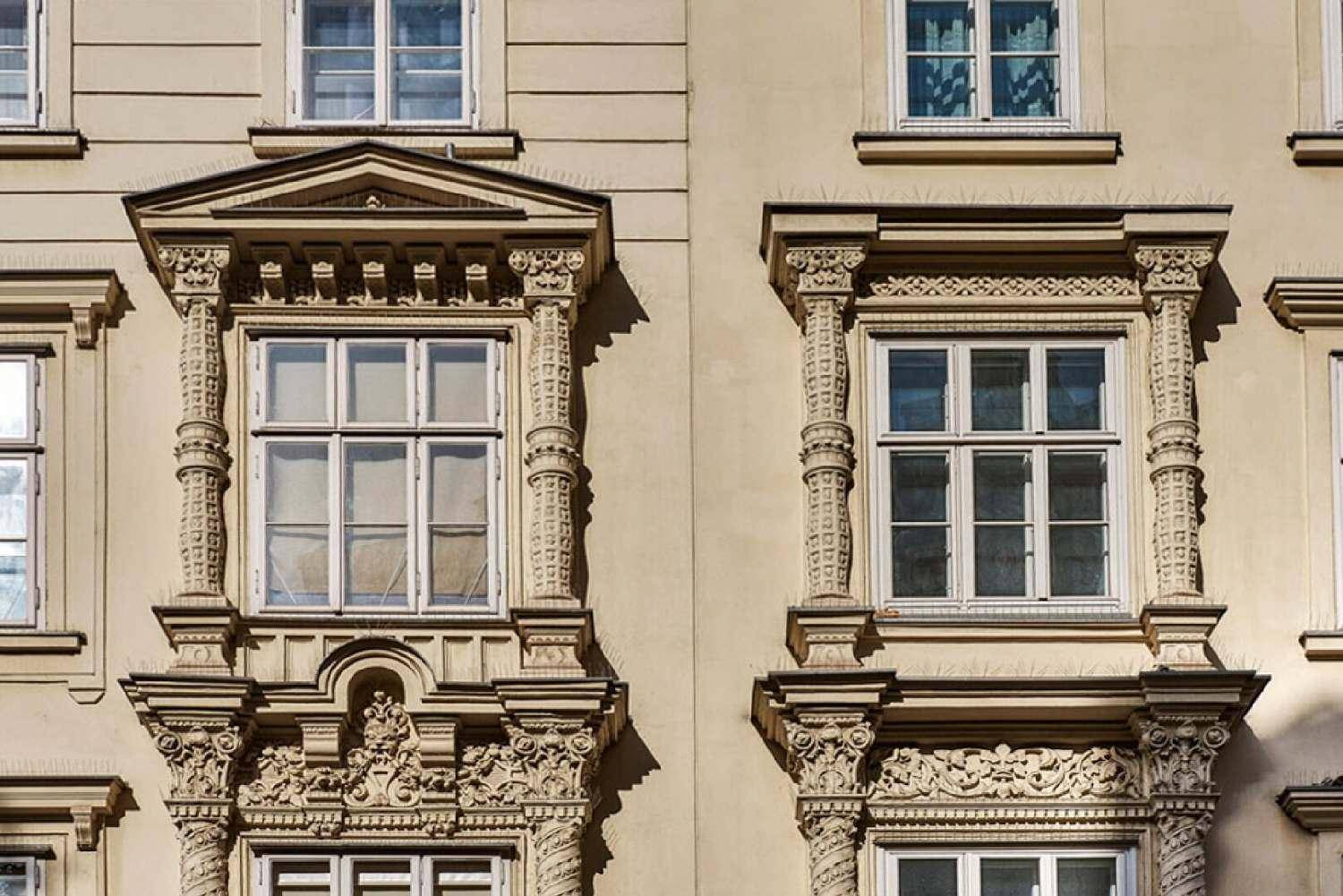 Nahaufnahme der kunstvollen Fensterrahmen und detaillierten Stuckverzierungen an der Fassade.