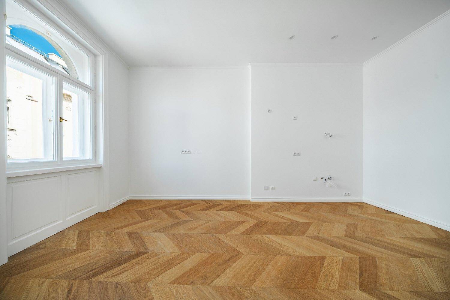Geräumiges Zimmer mit elegantem Fischgrätparkett und großen, bogenförmigen Fenstern.
