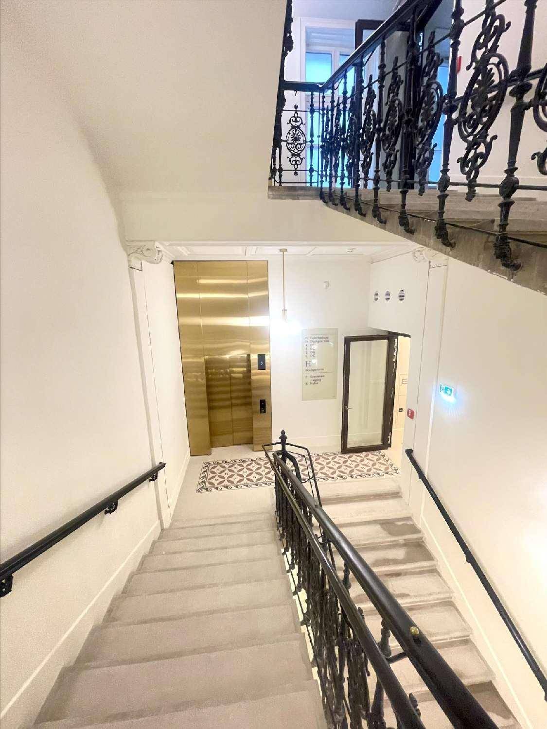 Elegantes Treppenhaus mit schmiedeeisernem Geländer und Blick auf den modernen Aufzug im Erdgeschoss.