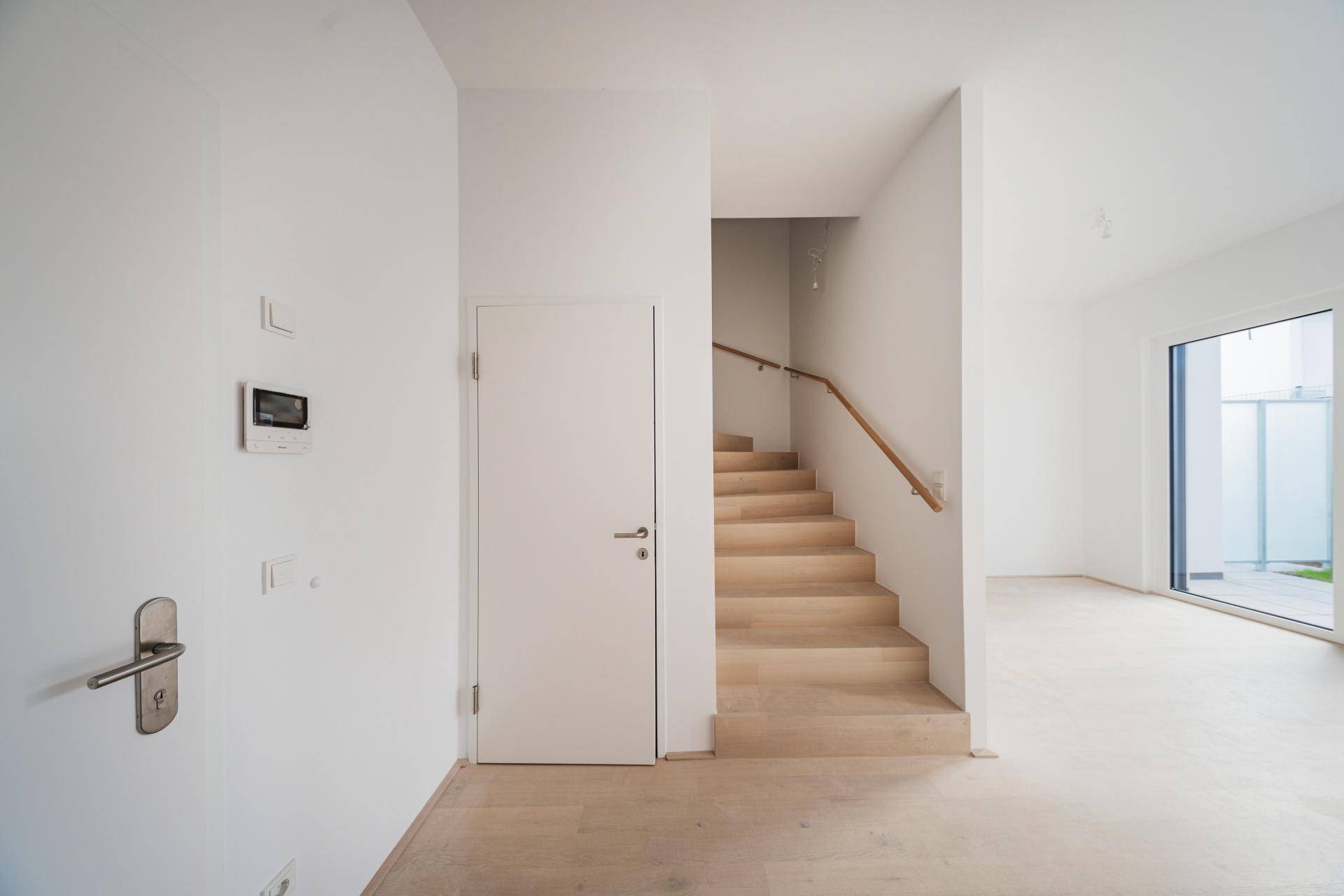 Heller Eingangsbereich mit moderner Tür, Holztreppe und Zugang zu den Wohnräumen.