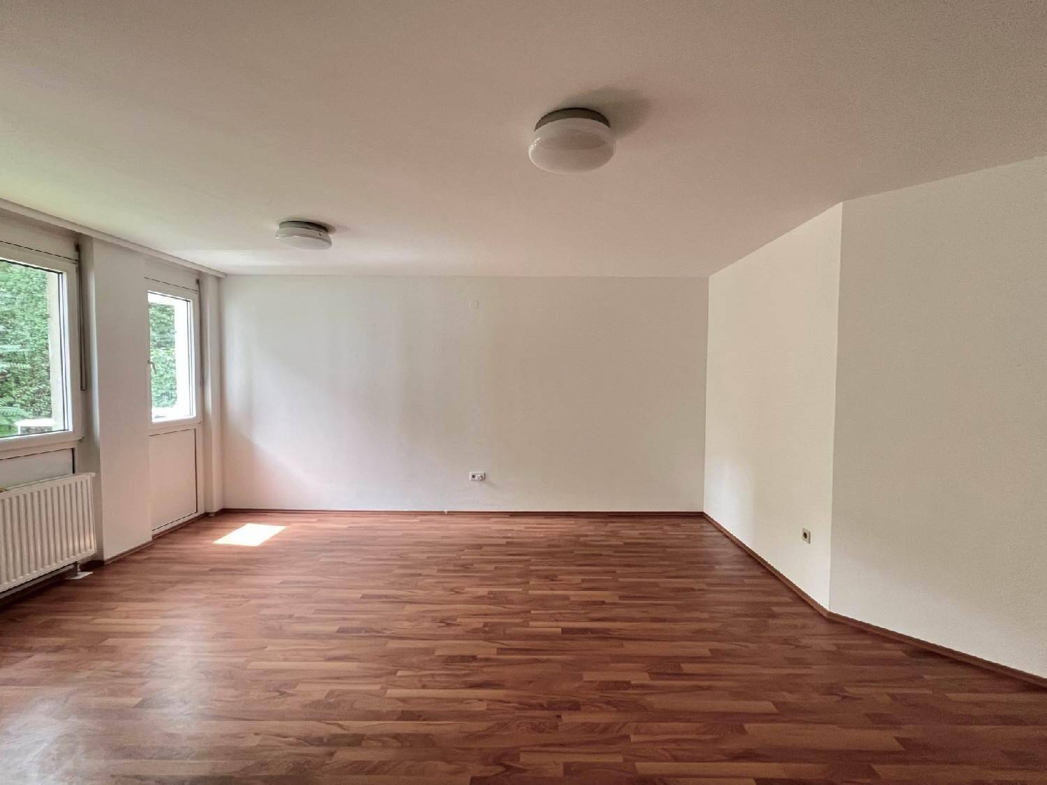 Geräumiger, heller Wohnbereich mit Holzboden und großen Fenstern, die viel Tageslicht hereinlassen.