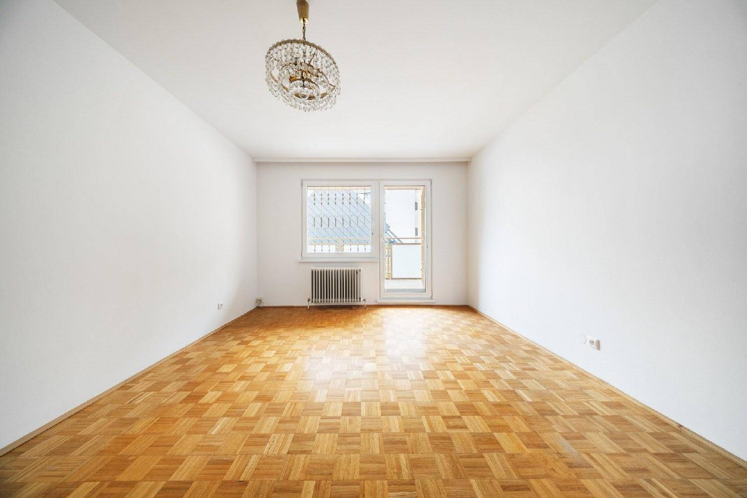 Leeres Zimmer mit Parkettboden, Kronleuchter und Fenster, bereit zur individuellen Gestaltung.