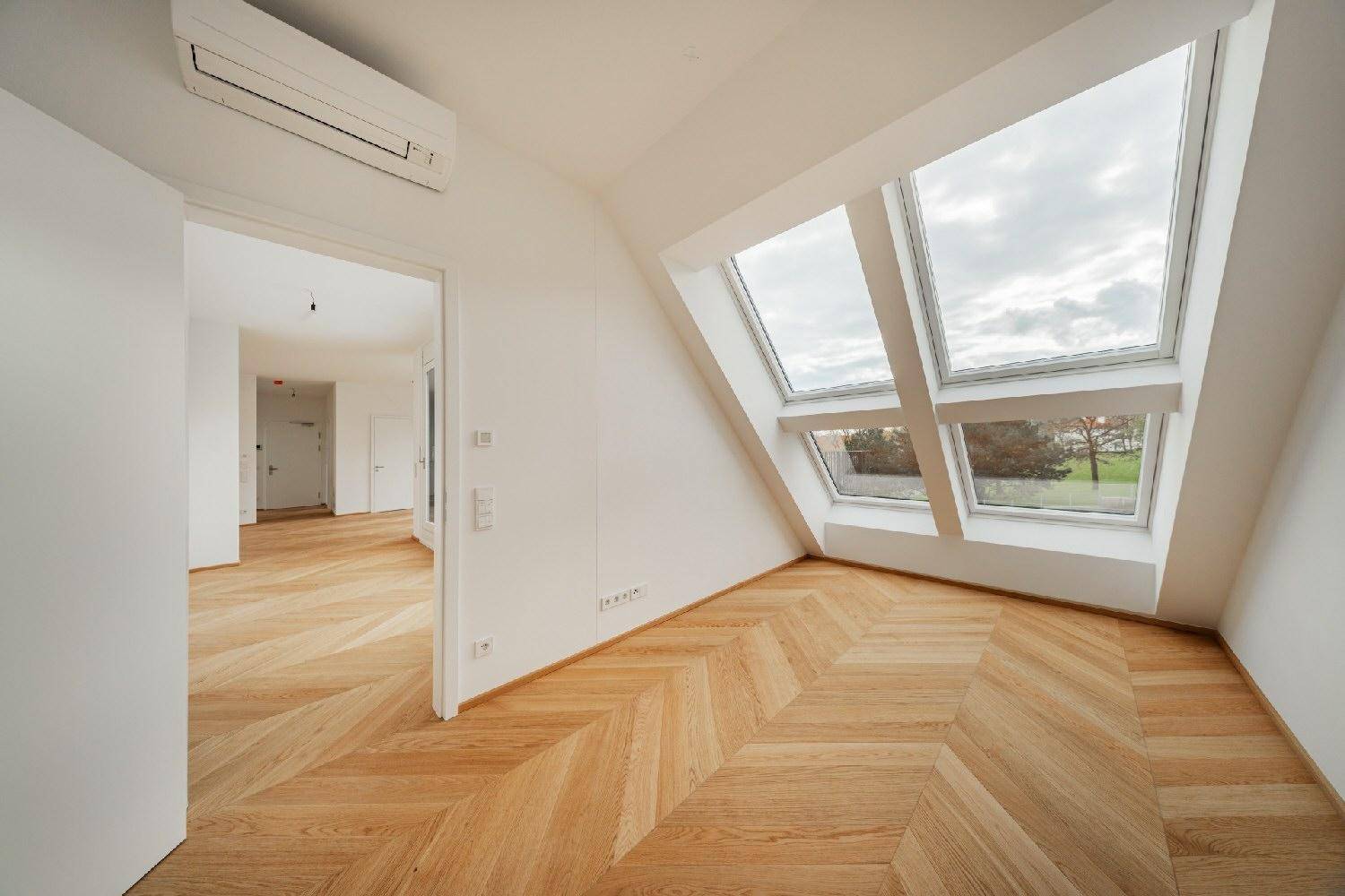 Lichtdurchflutetes Dachzimmer mit schrägem Dach, großen Fenstern und modernem Parkettboden im Neubau.