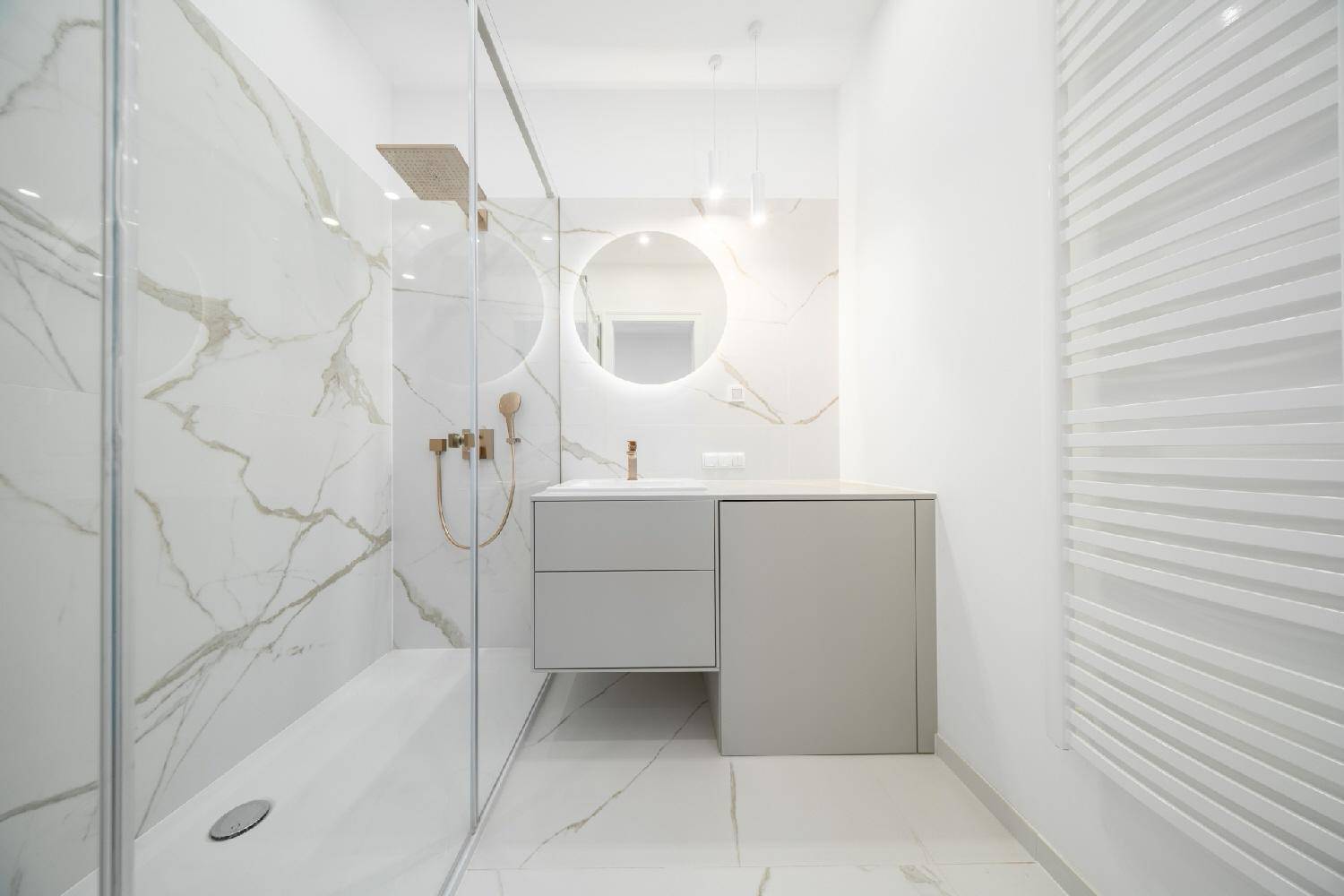 Modernes Badezimmer mit Marmorfliesen, begehbarer Dusche und einem elegant beleuchteten Spiegel.