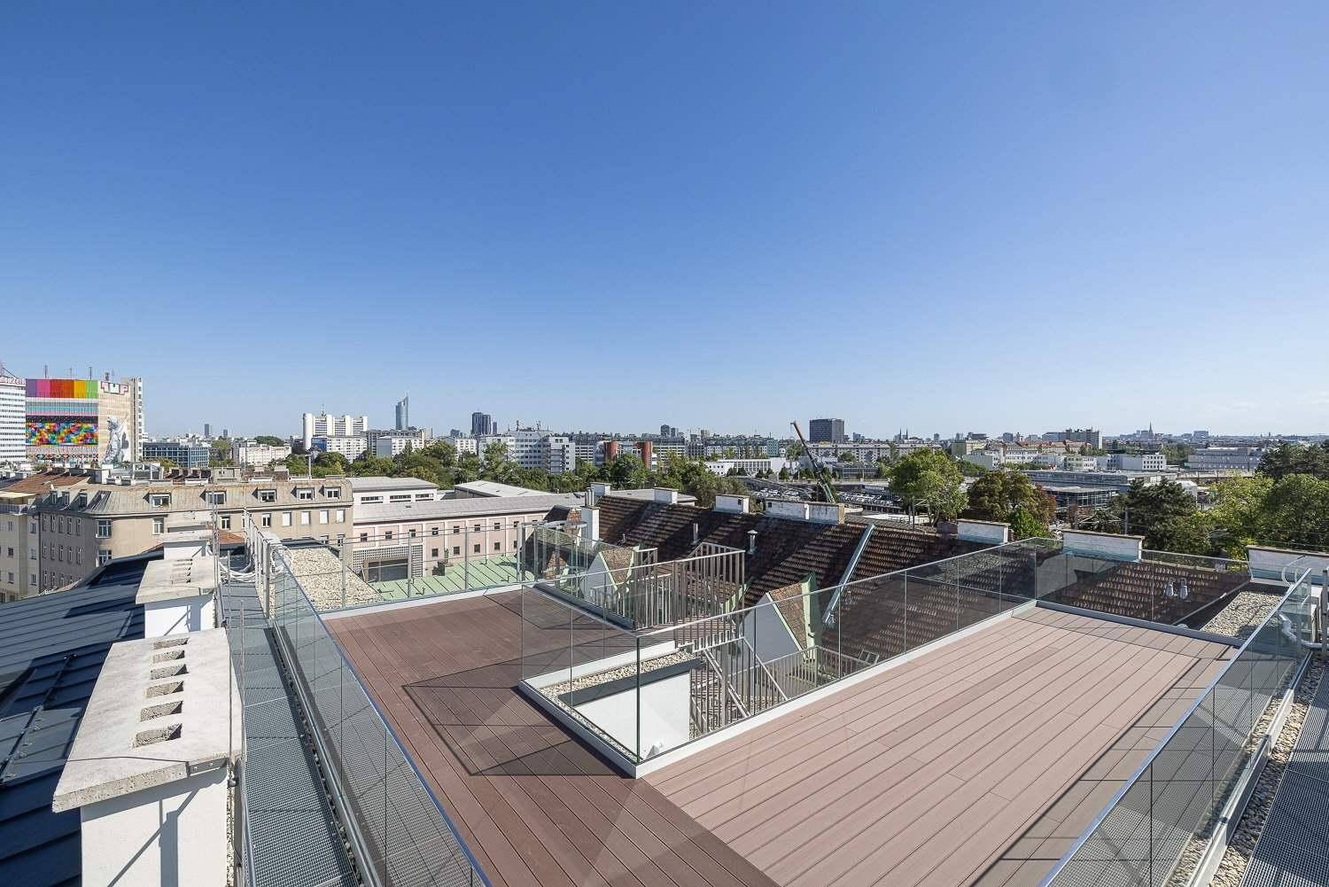 Panoramablick von der Dachterrasse mit Holzbelag und Glasgeländer über die Stadtlandschaft.