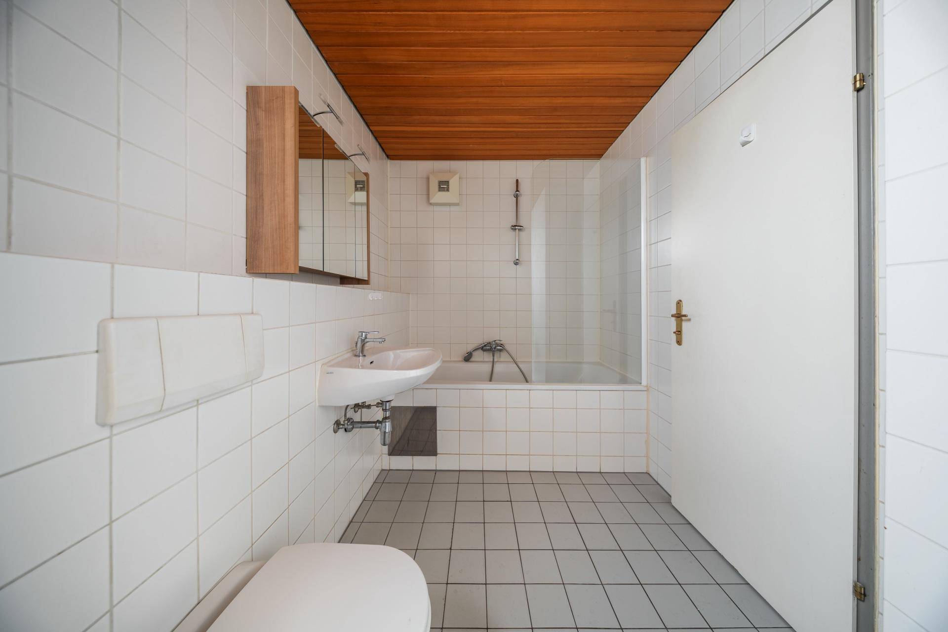 Badezimmer mit Badewanne, WC, Waschbecken, weißen Fliesen und Holzdecke.