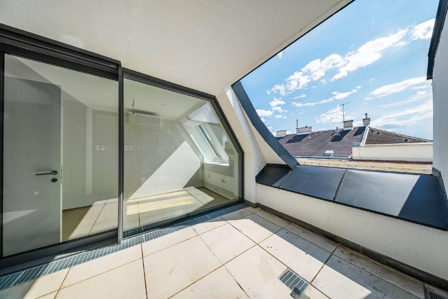 Sonnige Dachterrasse mit Fliesenboden und Blick über die umliegenden Dächer der Stadt.