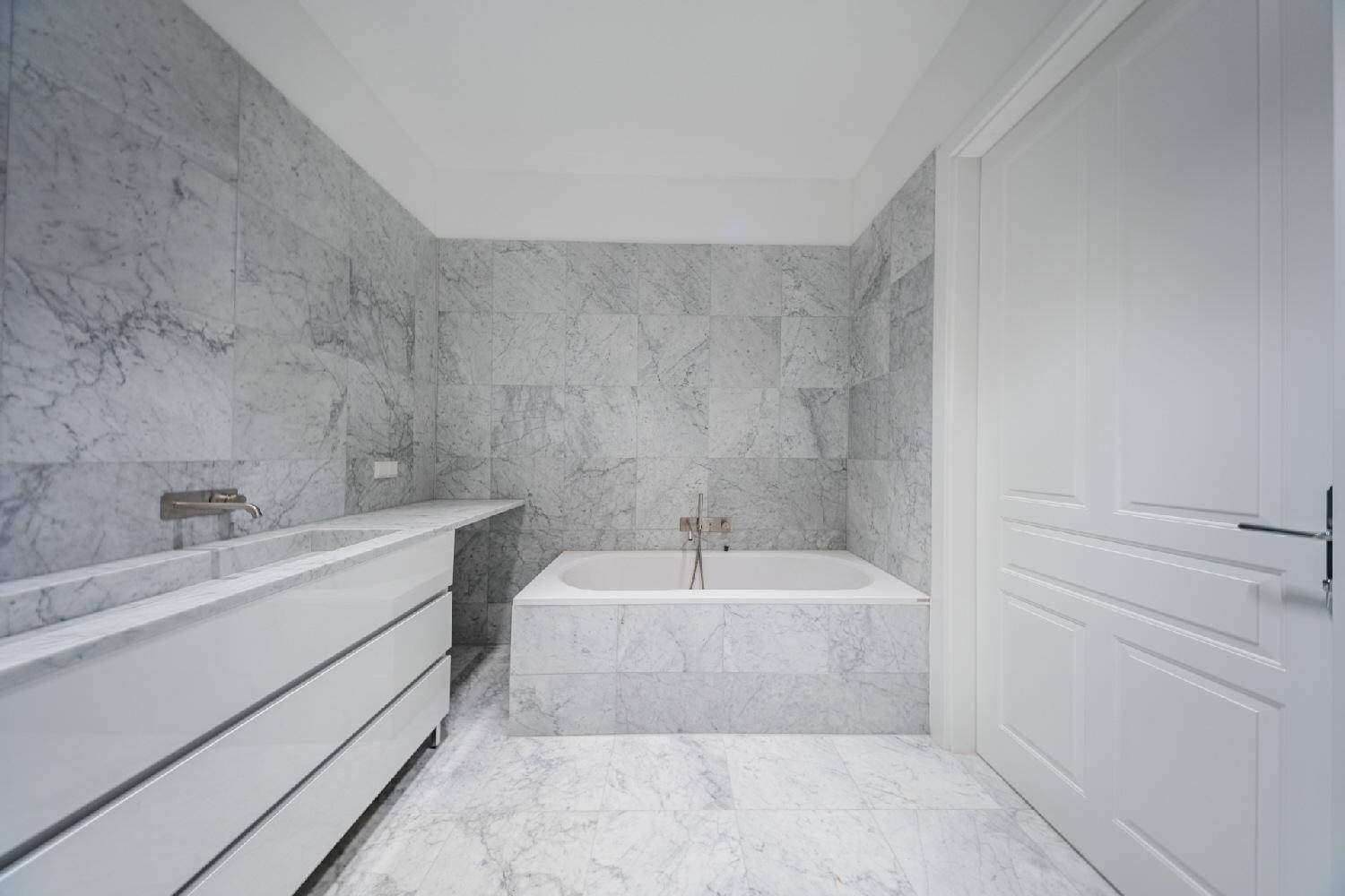 Elegantes Badezimmer mit Marmorfliesen, integrierter Badewanne und modernem Waschtisch.