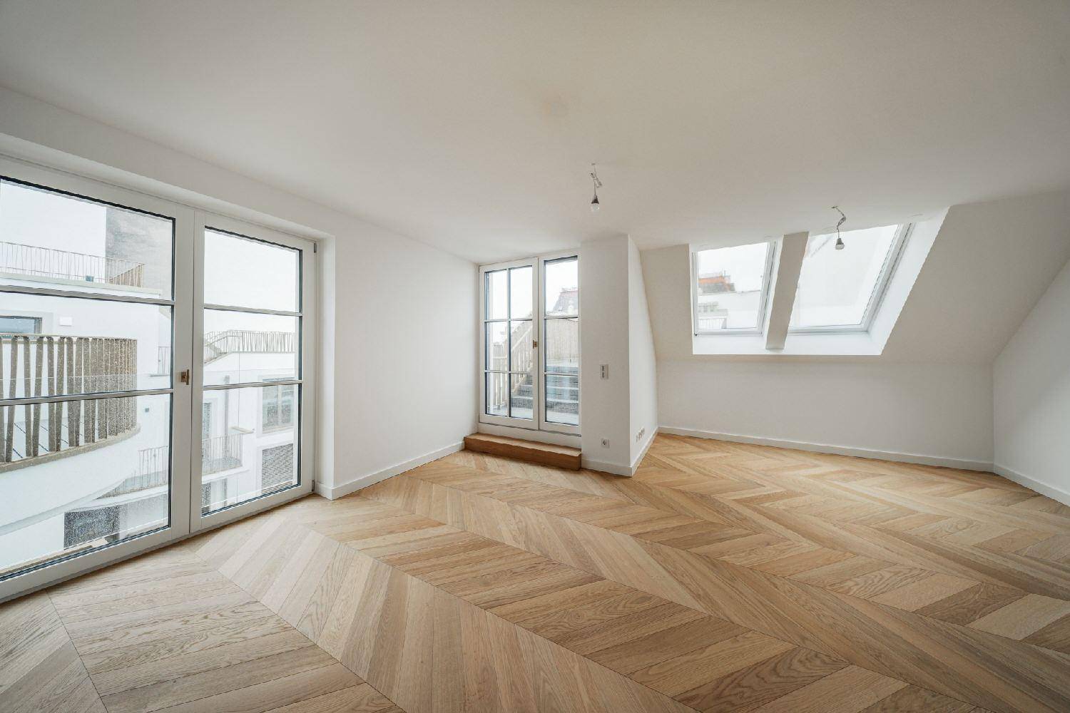Geräumiges Zimmer mit Fischgrätparkett, großen Fenstern und Dachfenstern für viel Tageslicht.
