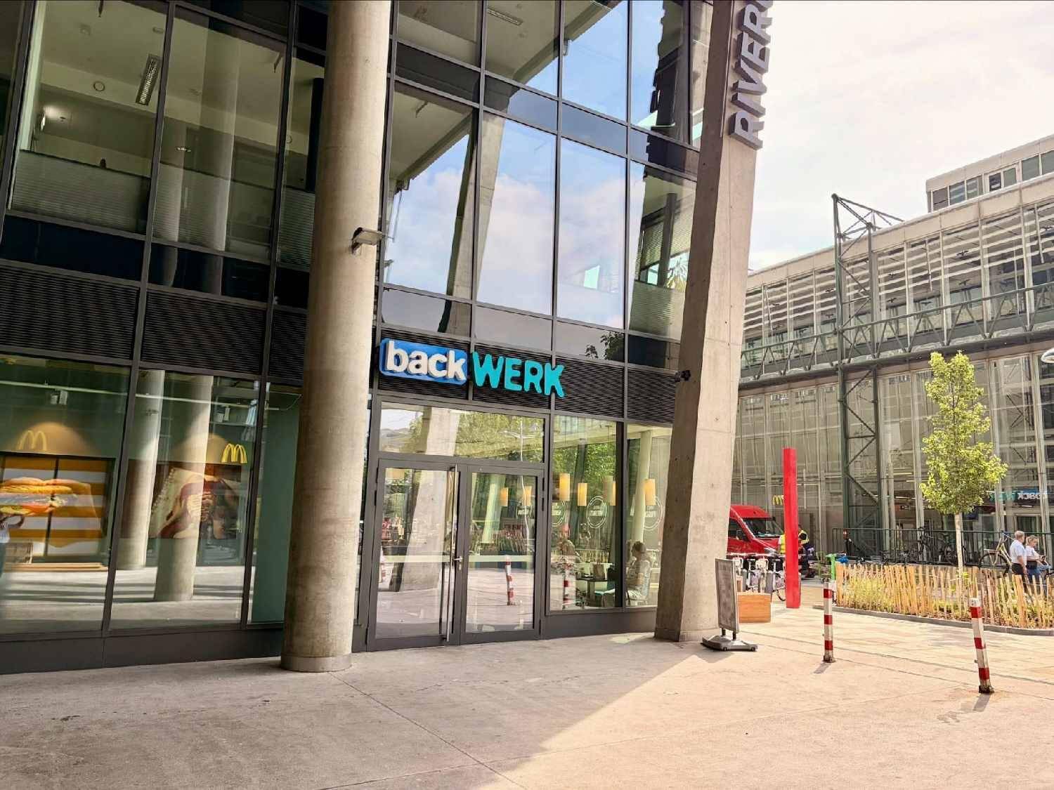 Eingangsbereich eines modernen Geschäftsgebäudes mit großen Glastüren und reflektierenden Fenstern.