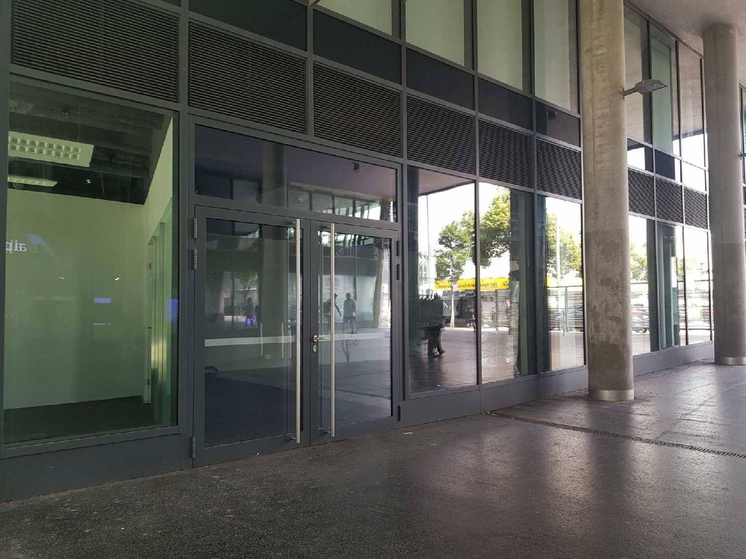 Eingangsbereich eines modernen Gebäudes mit großen Glasfenstern und grauen Rahmen.